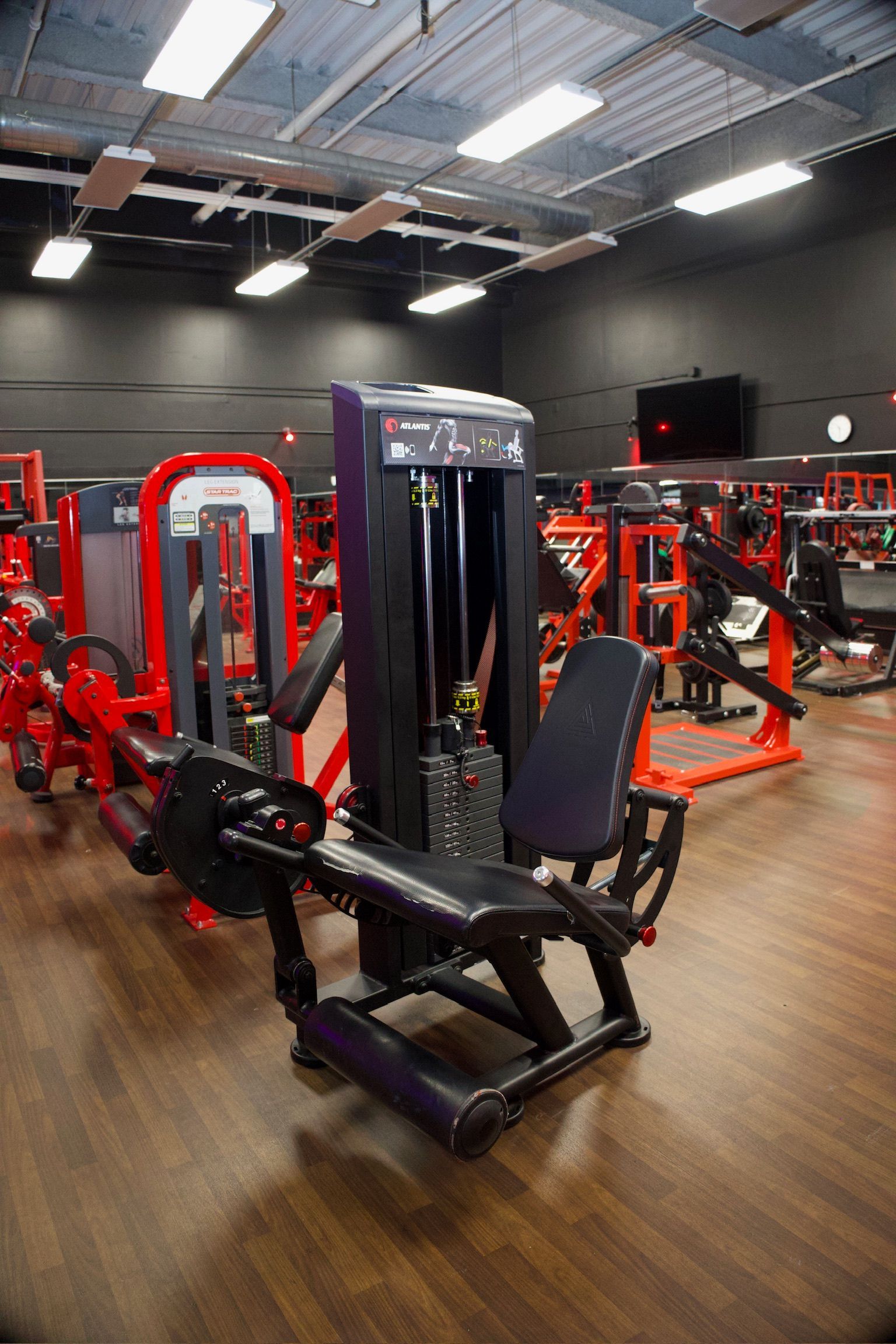 Gym with black and red exercise machines on a wooden floor.