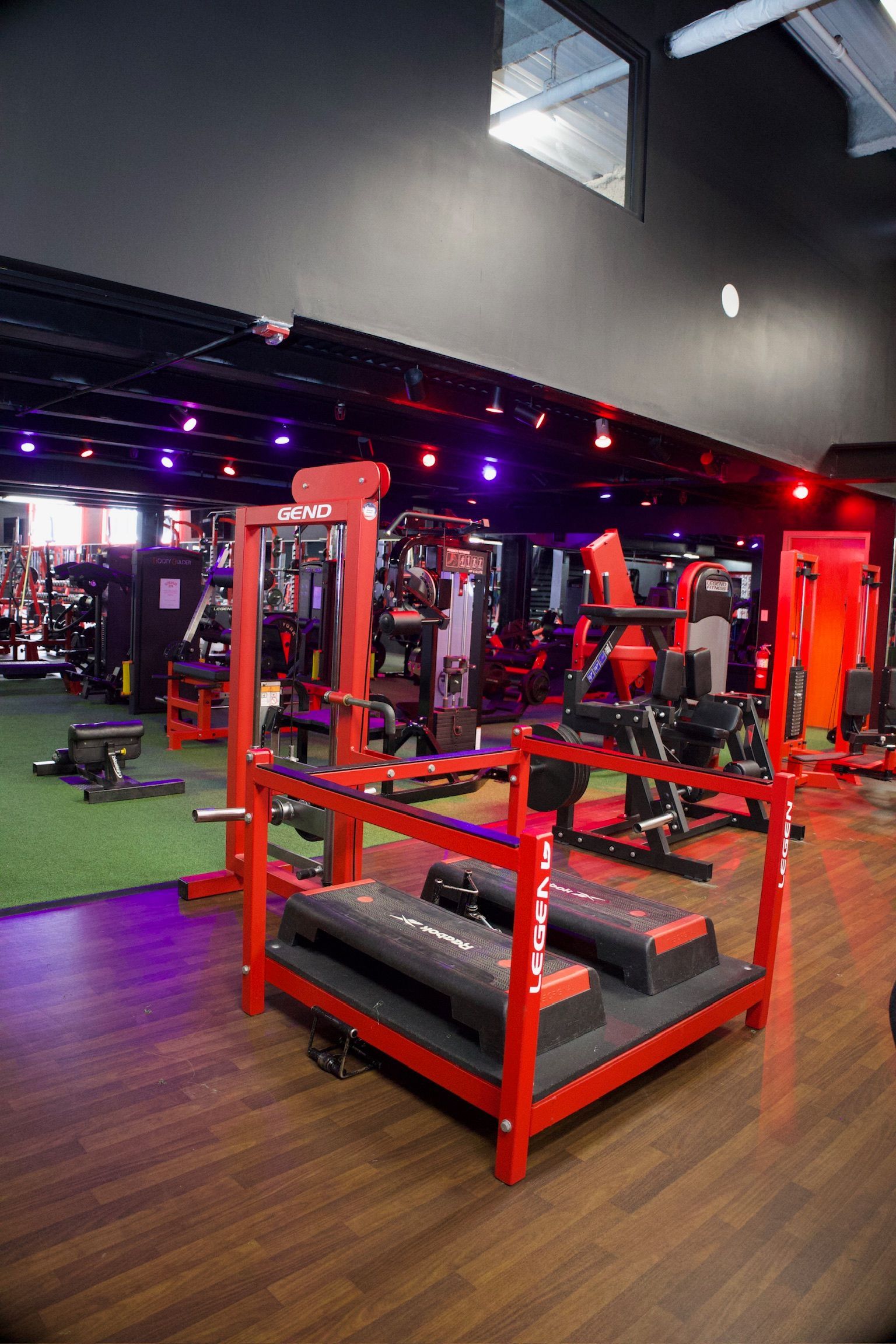 Red gym equipment in a brightly lit gym. Wood floor, black ceiling, artificial turf.