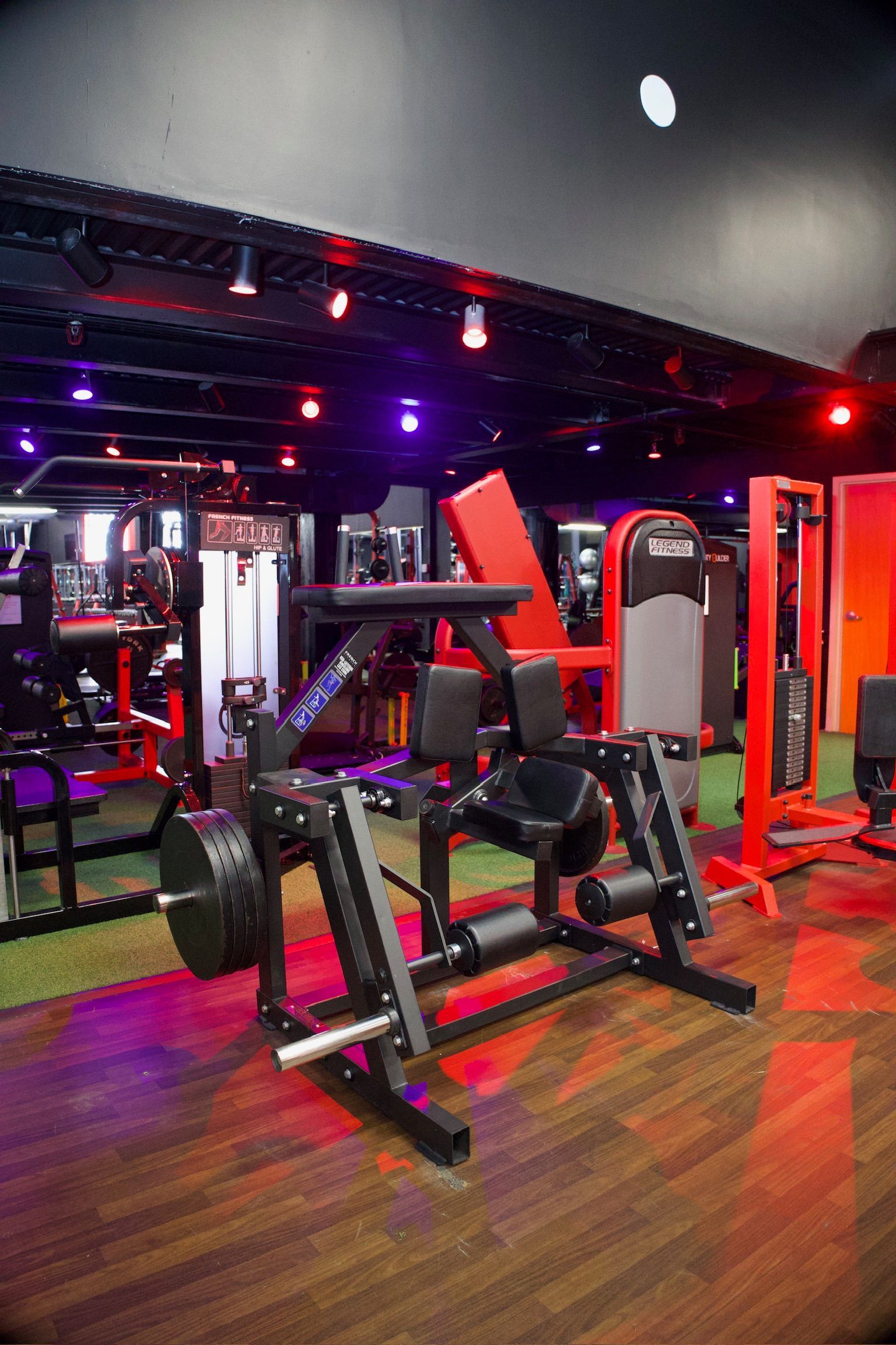 Gym interior with weight machines, red and black equipment, and colorful lighting.