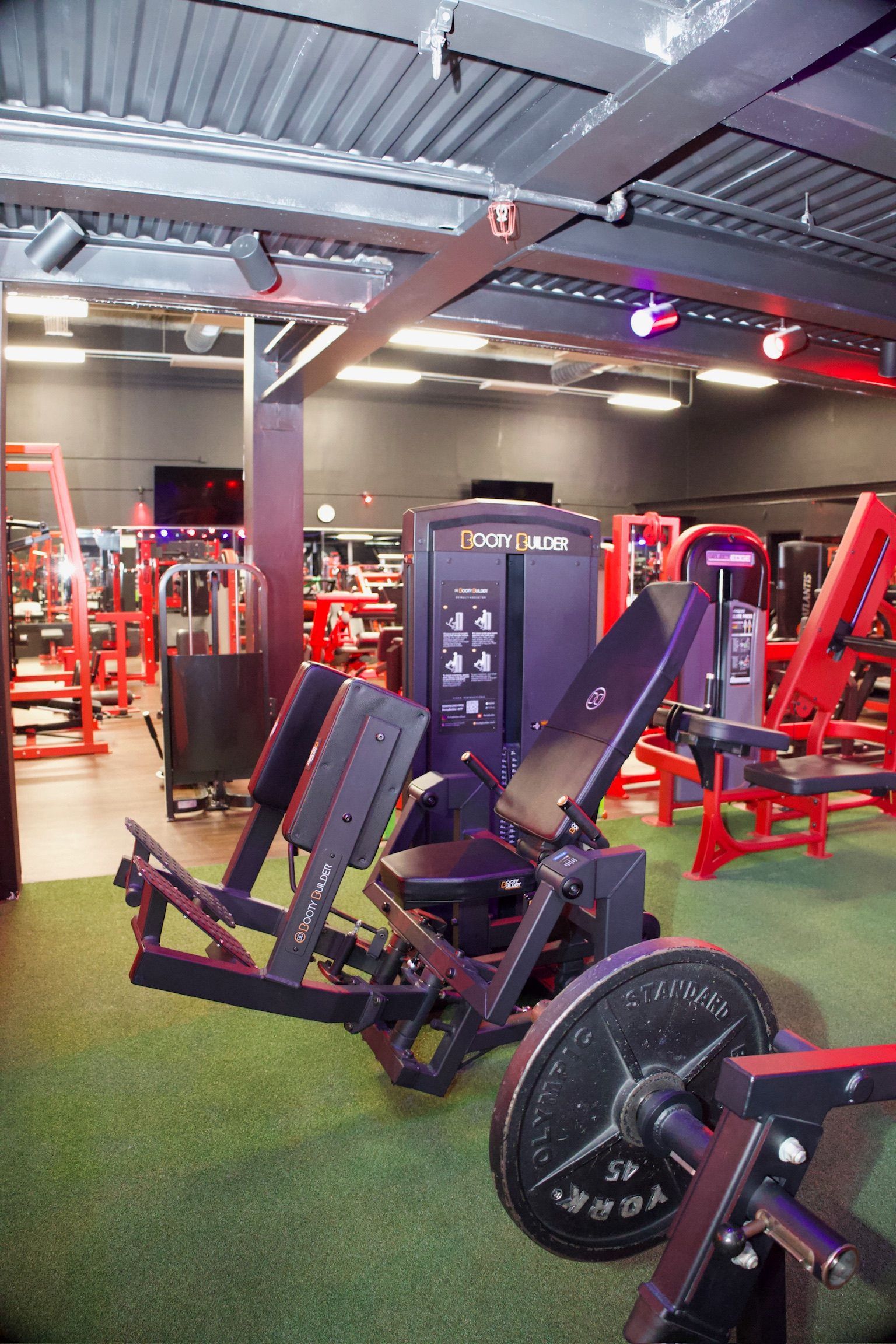 Weight machine in gym with black and red equipment on green turf.