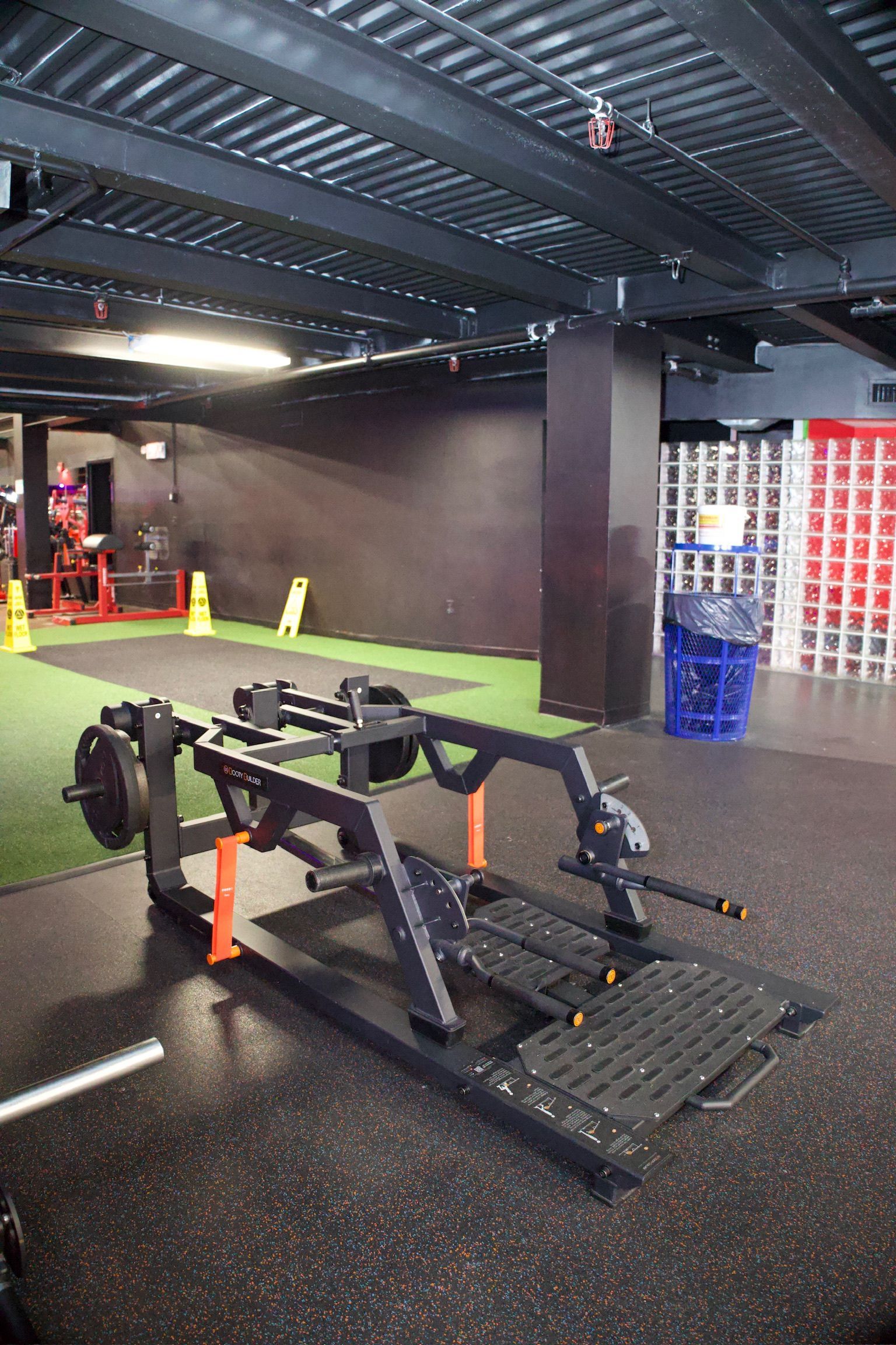Weight machine in a gym, with a black frame, orange accents, and weight plates, on a black floor.