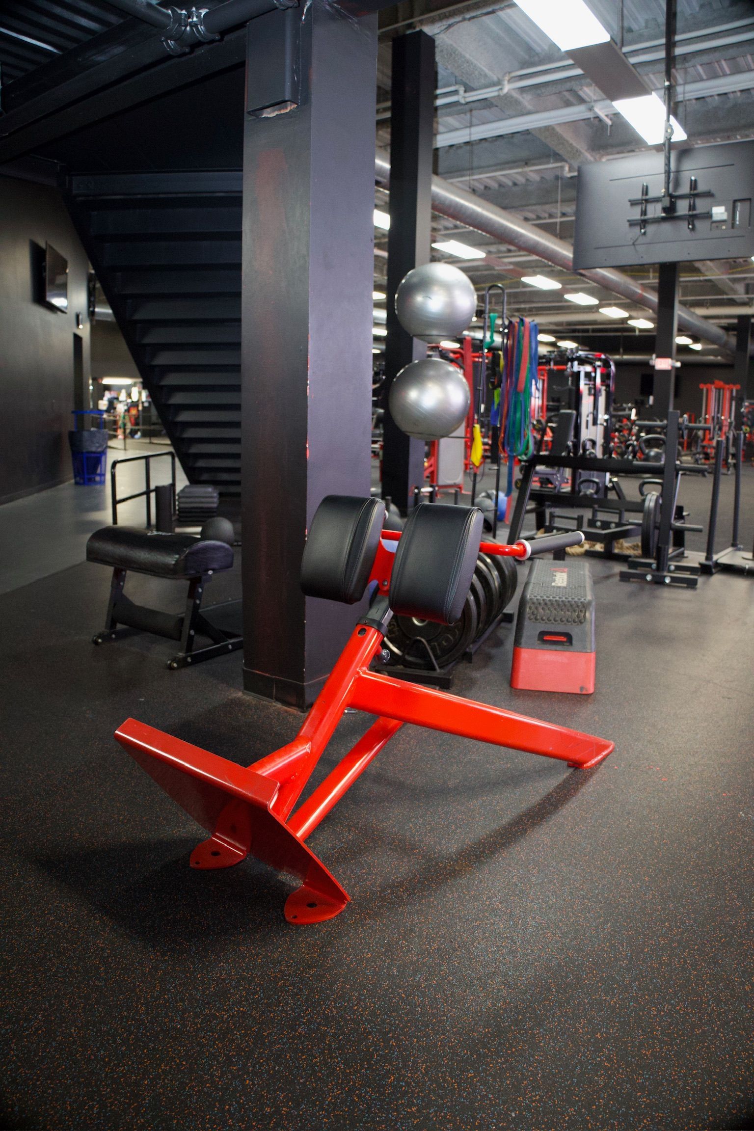 Red weight bench in a gym with weights, stairs, and fitness equipment.