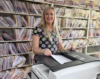 Woman standing at copy machine with files behind her 