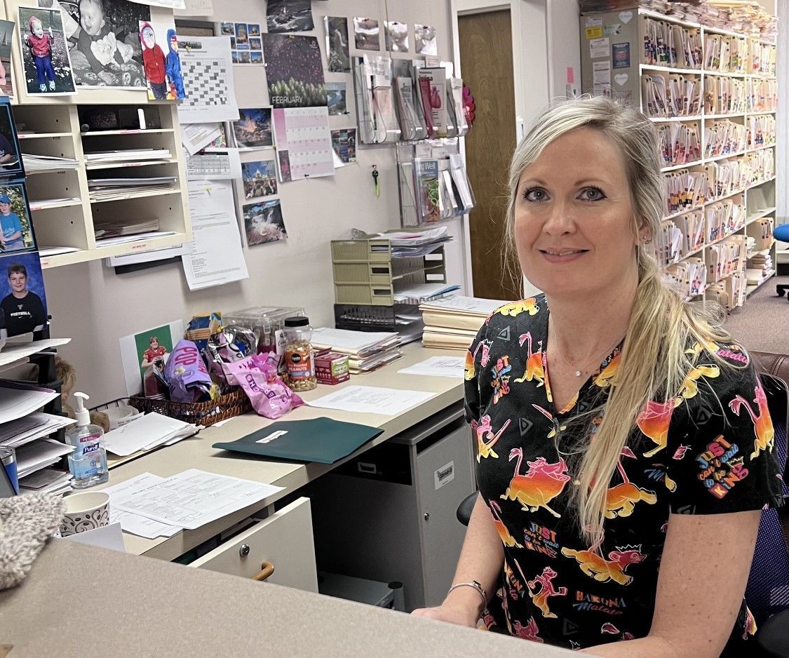 a woman in a scrub top is sitting at a desk