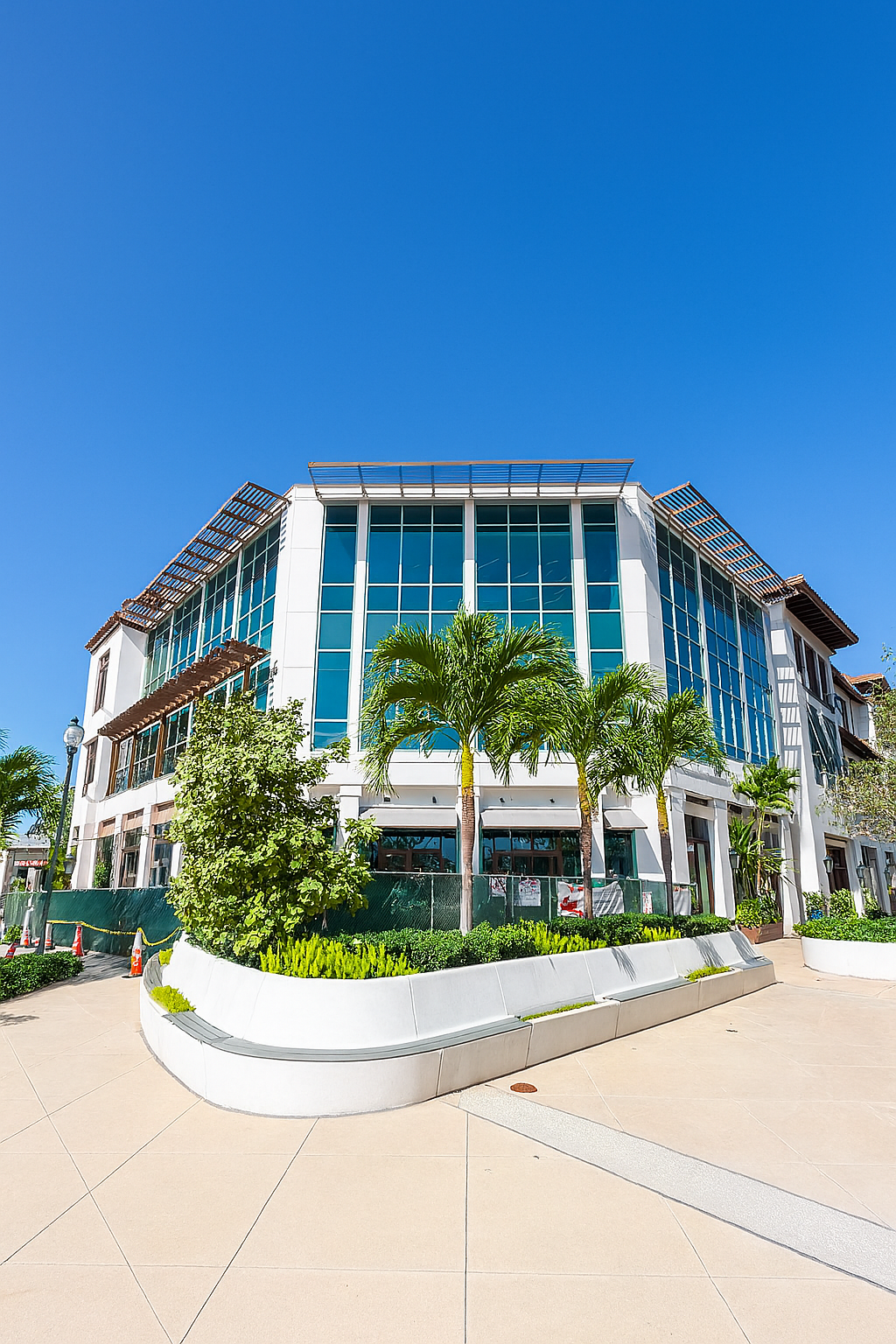 Modern white building with large windows and landscaping, against a bright blue sky.