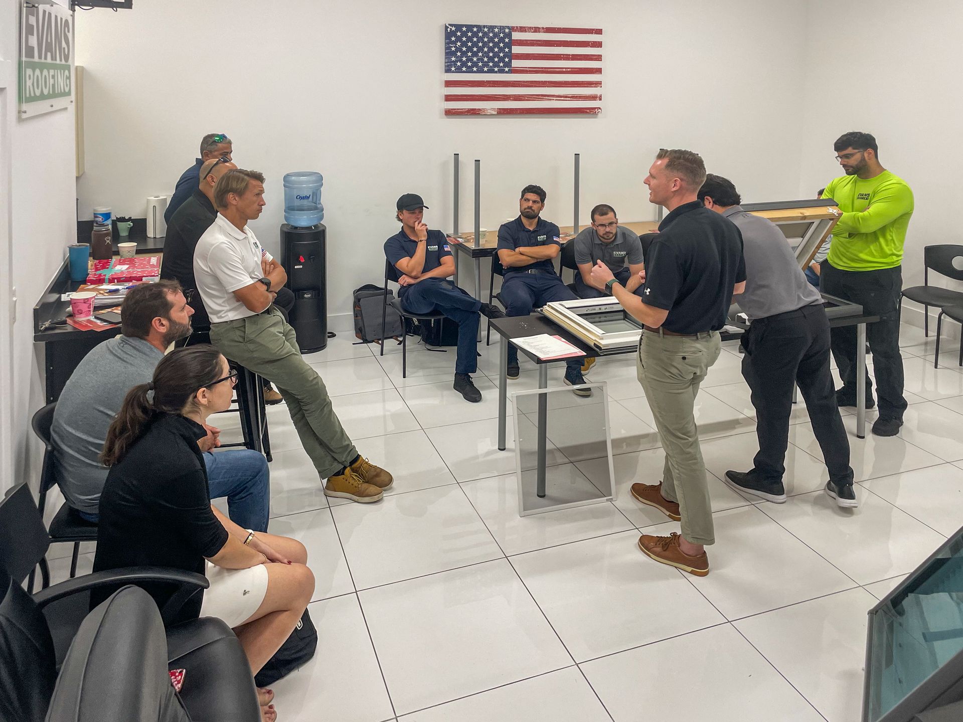 A group of people are sitting around a table in a room with an american flag on the wall.