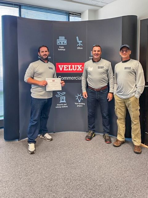 Three men are standing in front of a velux sign.