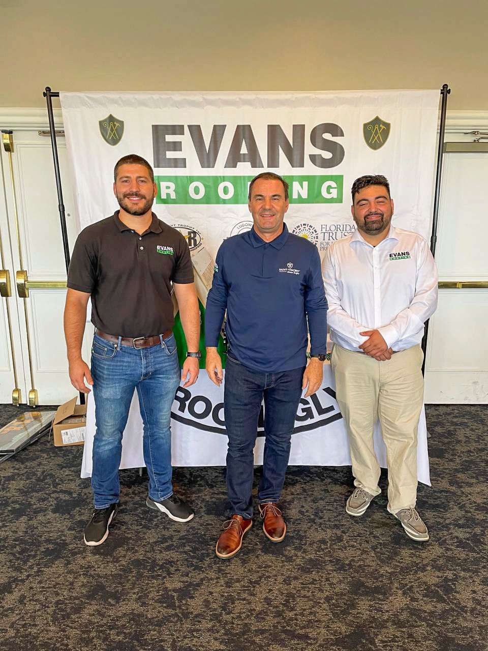 Three men are standing in front of a banner that says evans roofing.