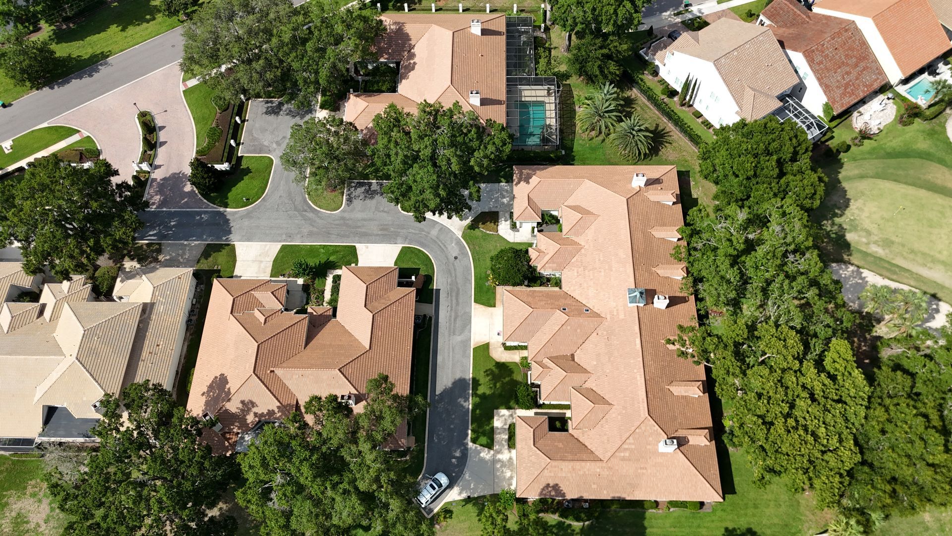 Aerial view of several houses with brown tile roofs, green lawns, and trees.