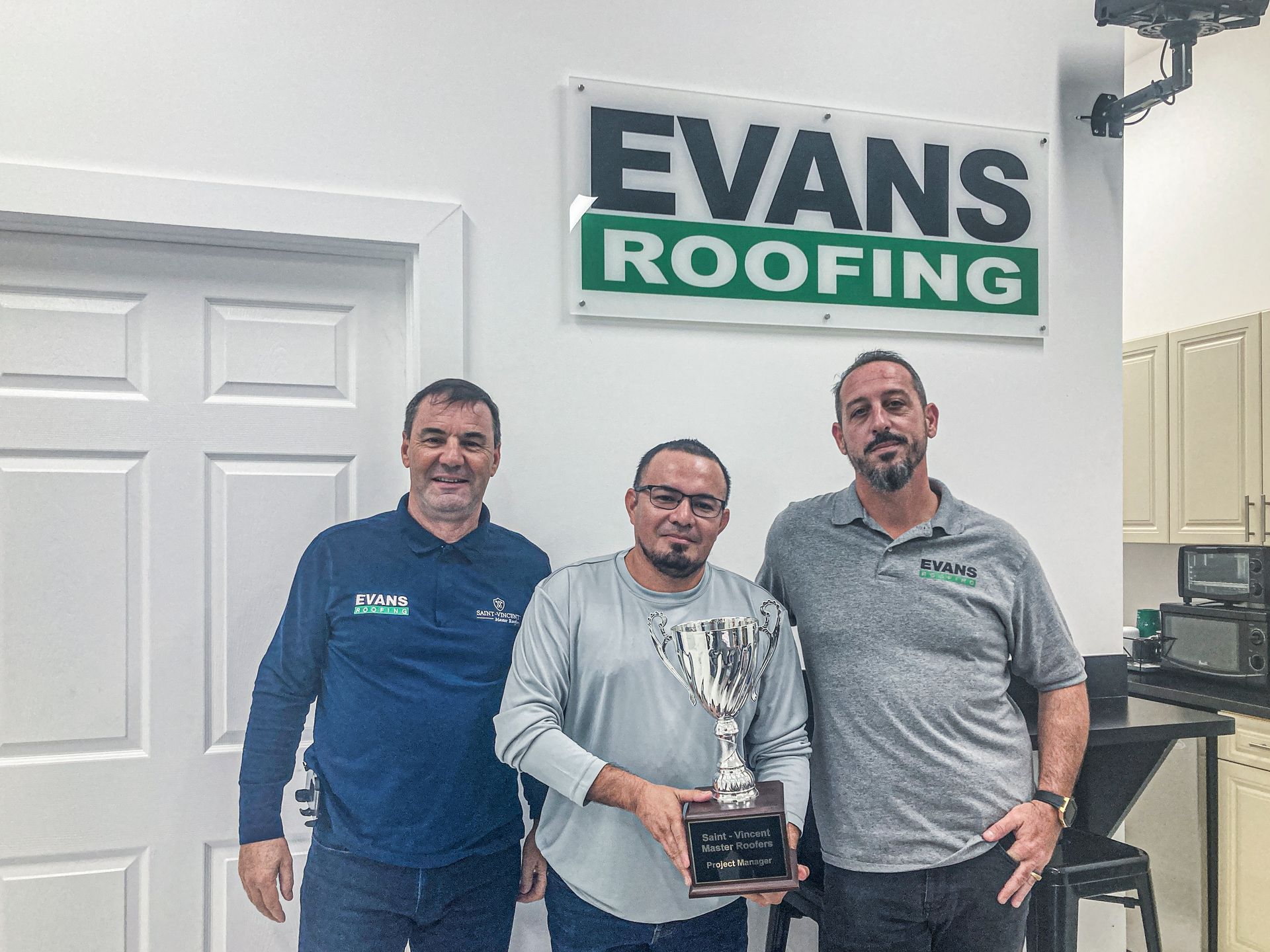 Three men are posing for a picture in front of a sign that says evans roofing.