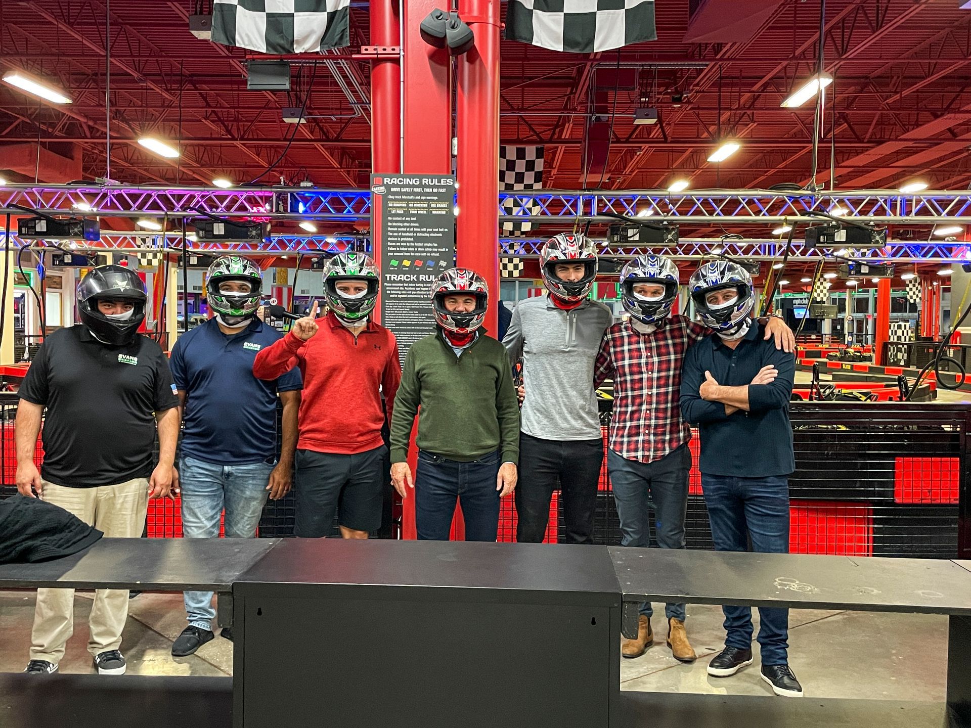 A group of men wearing go kart helmets are posing for a picture.