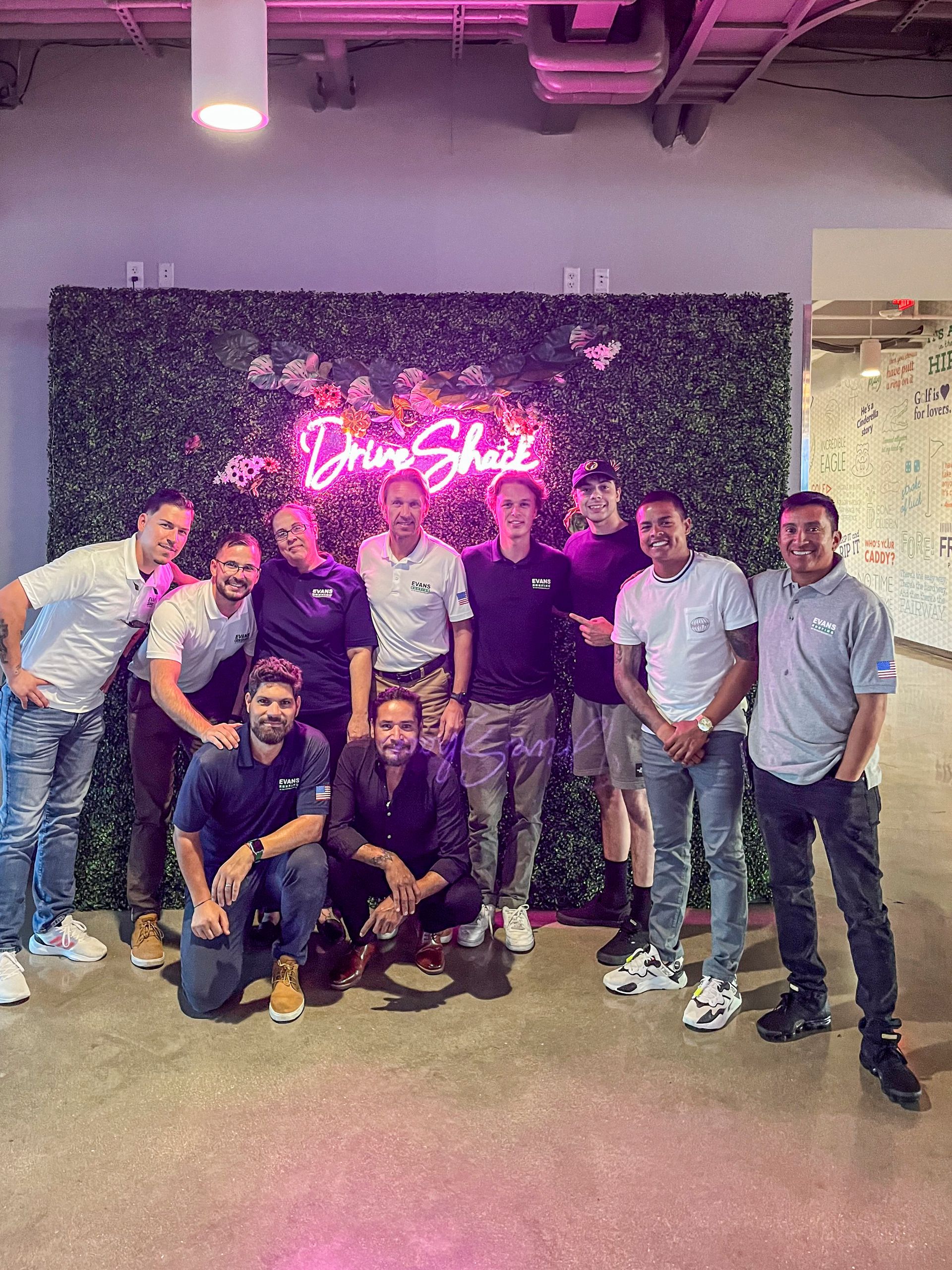 A group of men are posing for a picture in front of a neon sign.