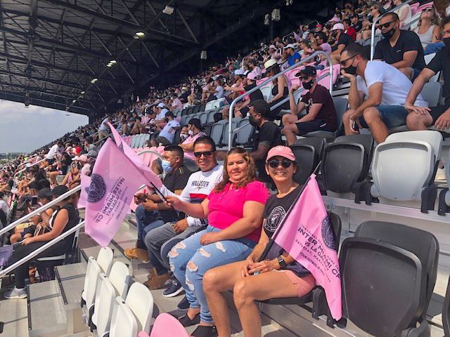 A group of people are sitting in a stadium holding pink flags.
