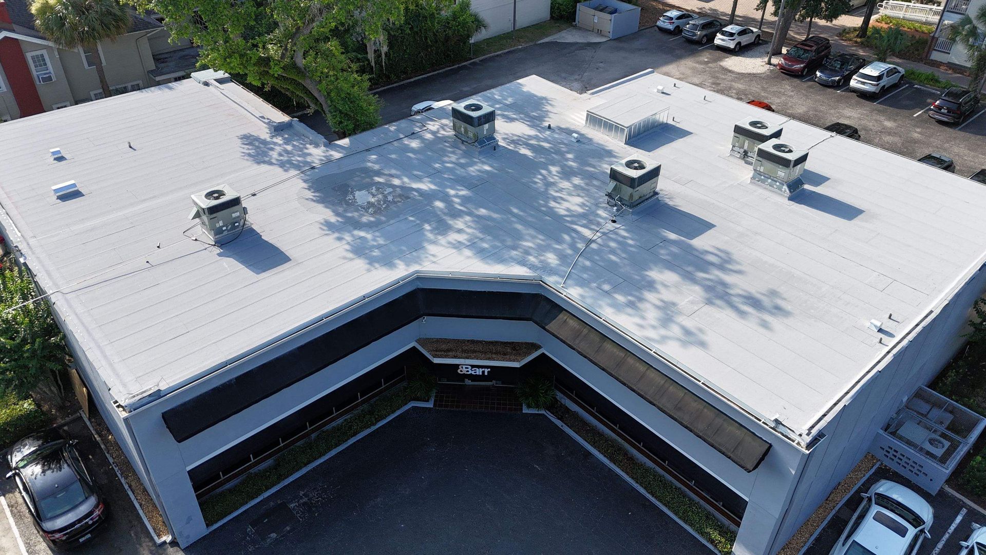 Aerial view of a gray, modern commercial building with a flat roof, several chimneys, and surrounding parking.