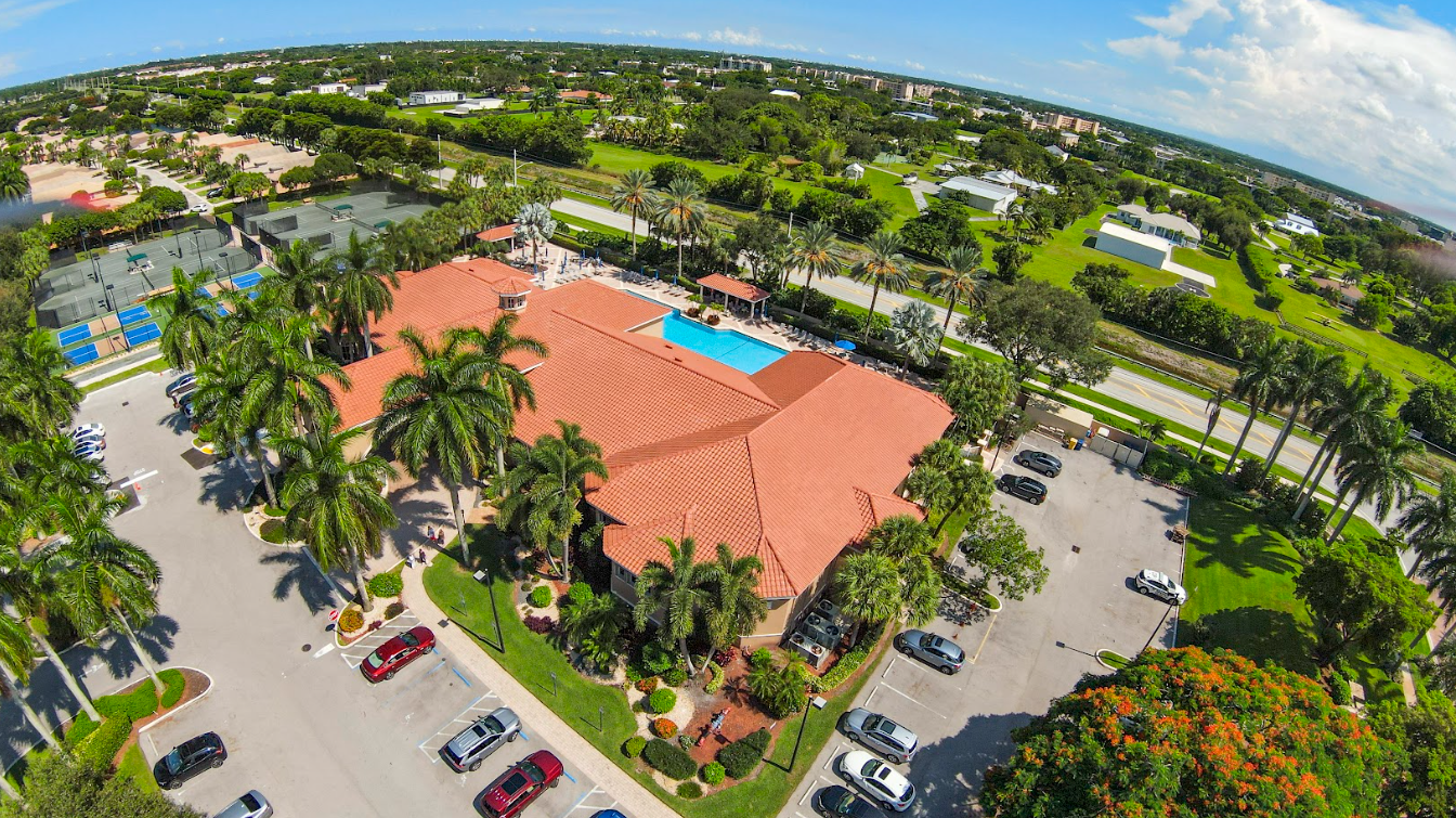 An aerial view of a clubhouse with a pool and a lot of cars parked in front of it