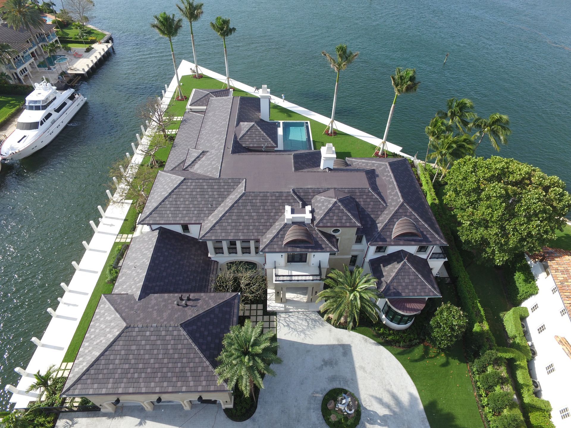 Aerial view of a luxury home on a waterway with a yacht, palm trees, and a swimming pool.