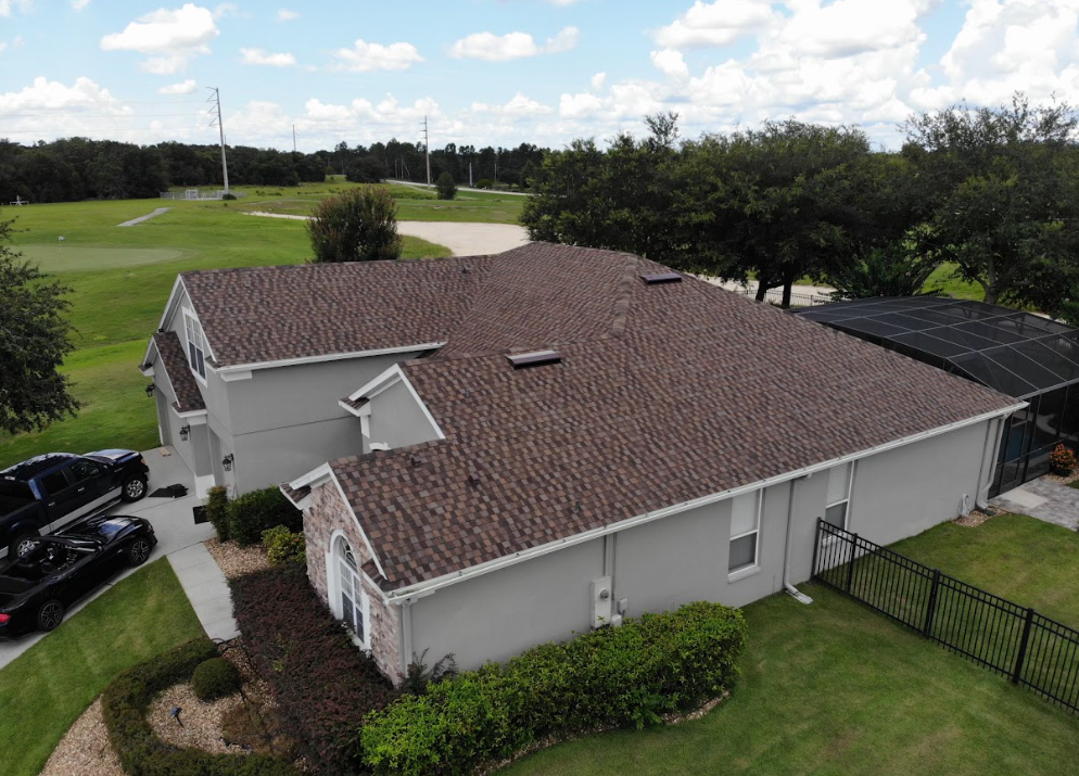An aerial view of a house with a brown roof and a golf course in the background