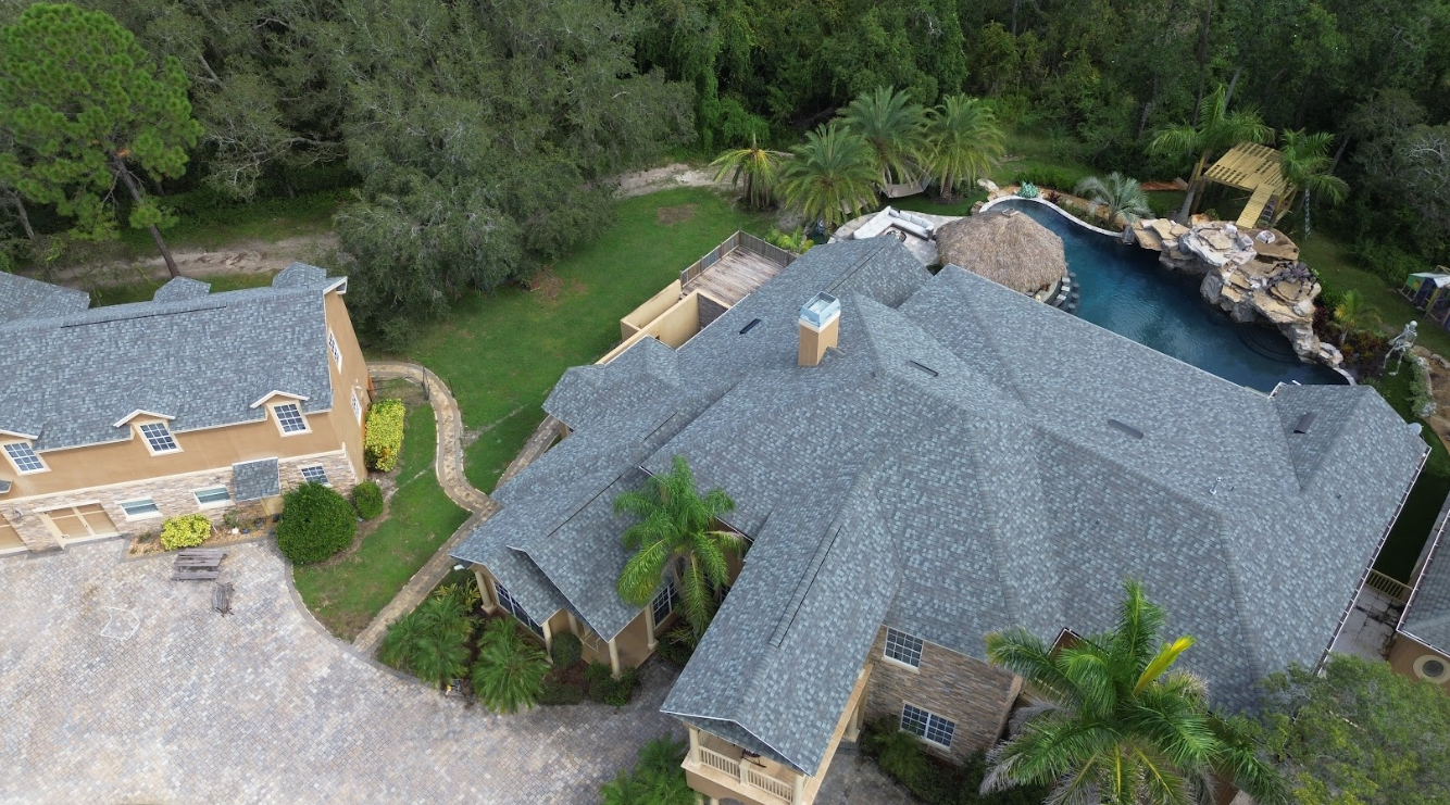 An aerial view of a large house with a pool in the backyard surrounded by trees