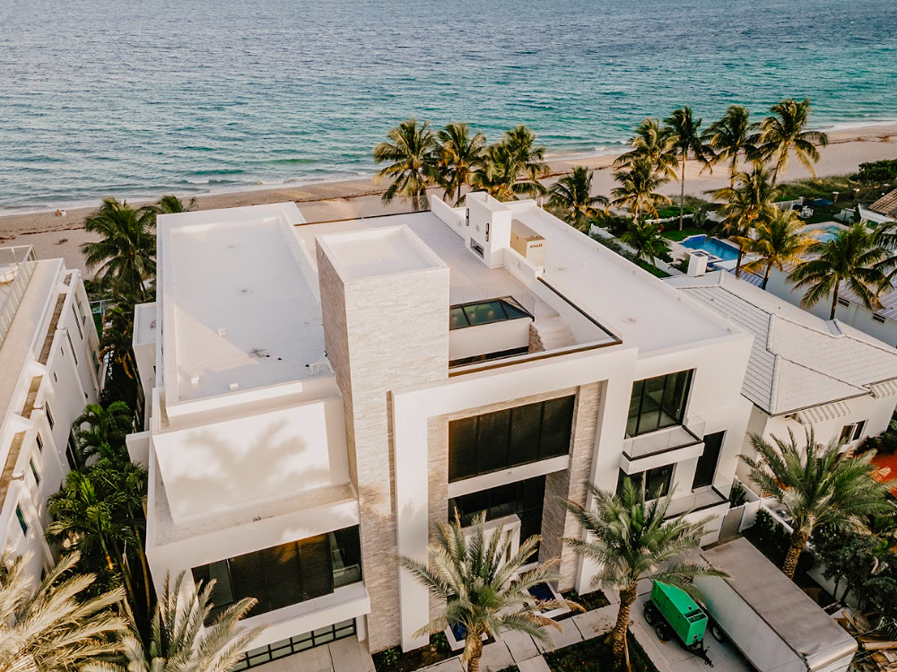 An aerial view of a large white house next to the ocean