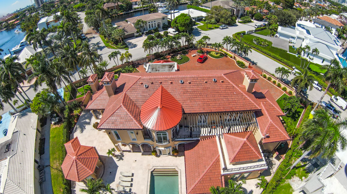 An aerial view of a large house with a red roof and a pool surrounded by palm trees