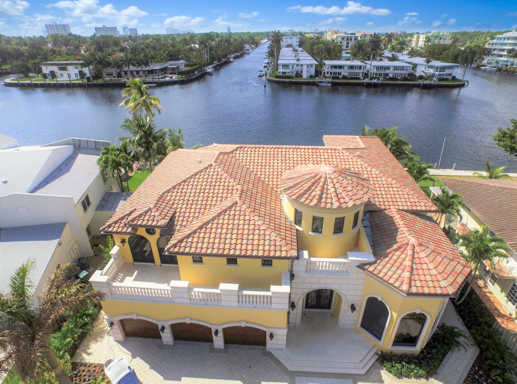 An aerial view of a large yellow house with a red tile roof surrounded by water