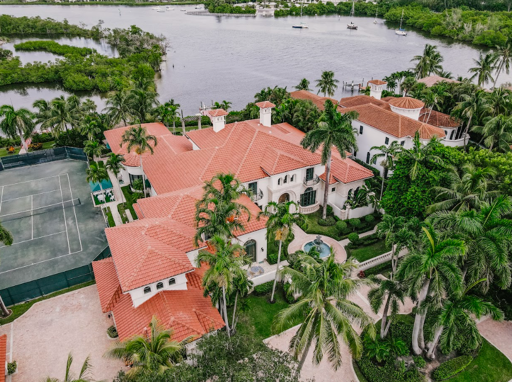 An aerial view of a large house surrounded by palm trees and a tennis court