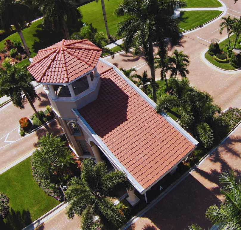 Large, white stucco mansion with red tile roof, palm trees, and a tennis court.