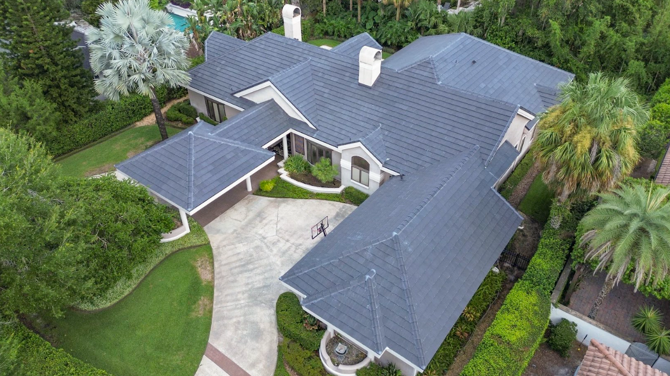 An aerial view of a large house with a blue roof surrounded by trees