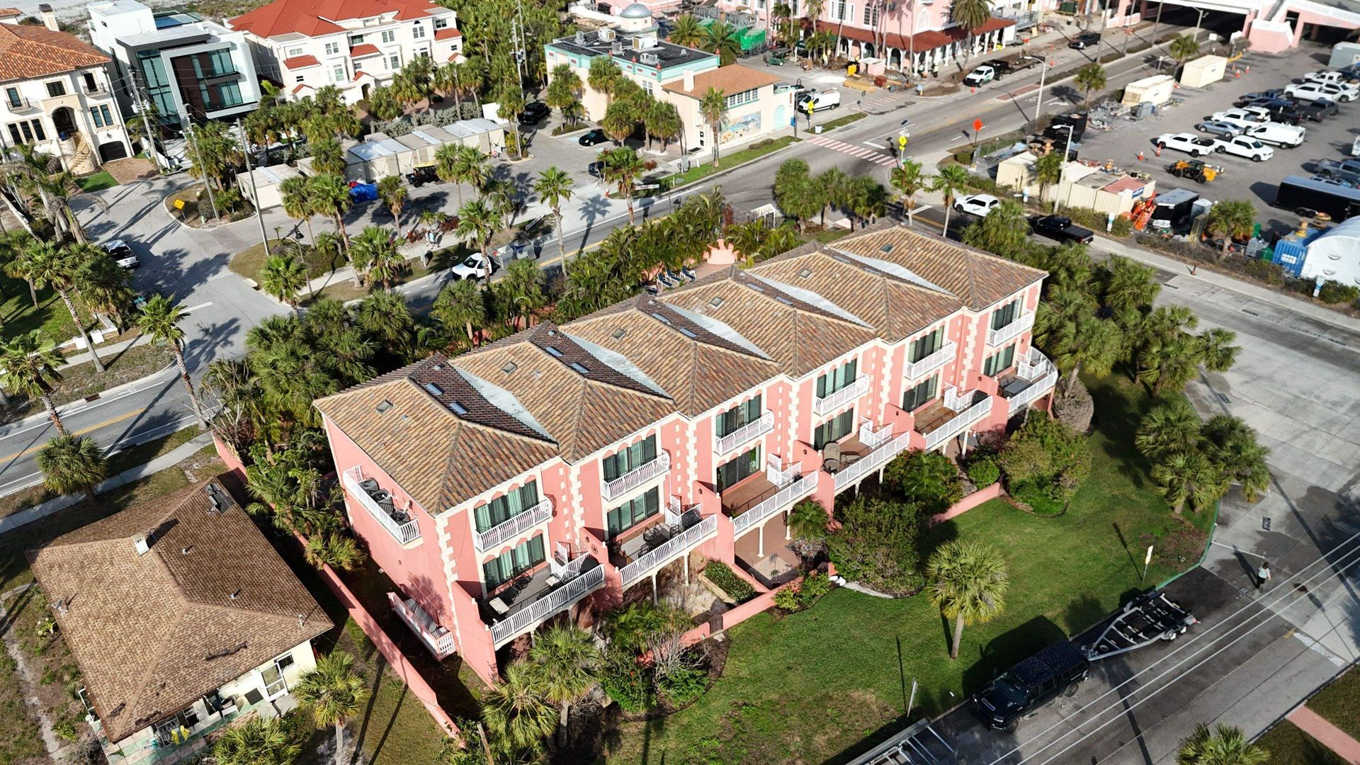 Aerial view of a pink building with several units, brown roof, next to a street with cars and other buildings.