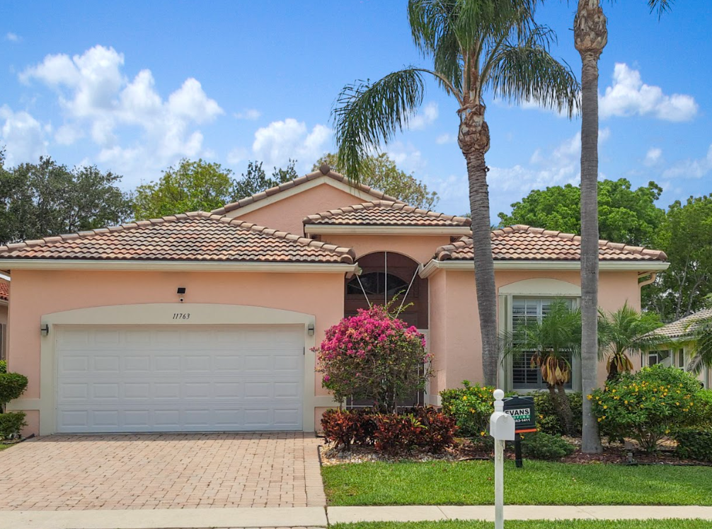 A pink house with a white garage door and a palm tree in front of it