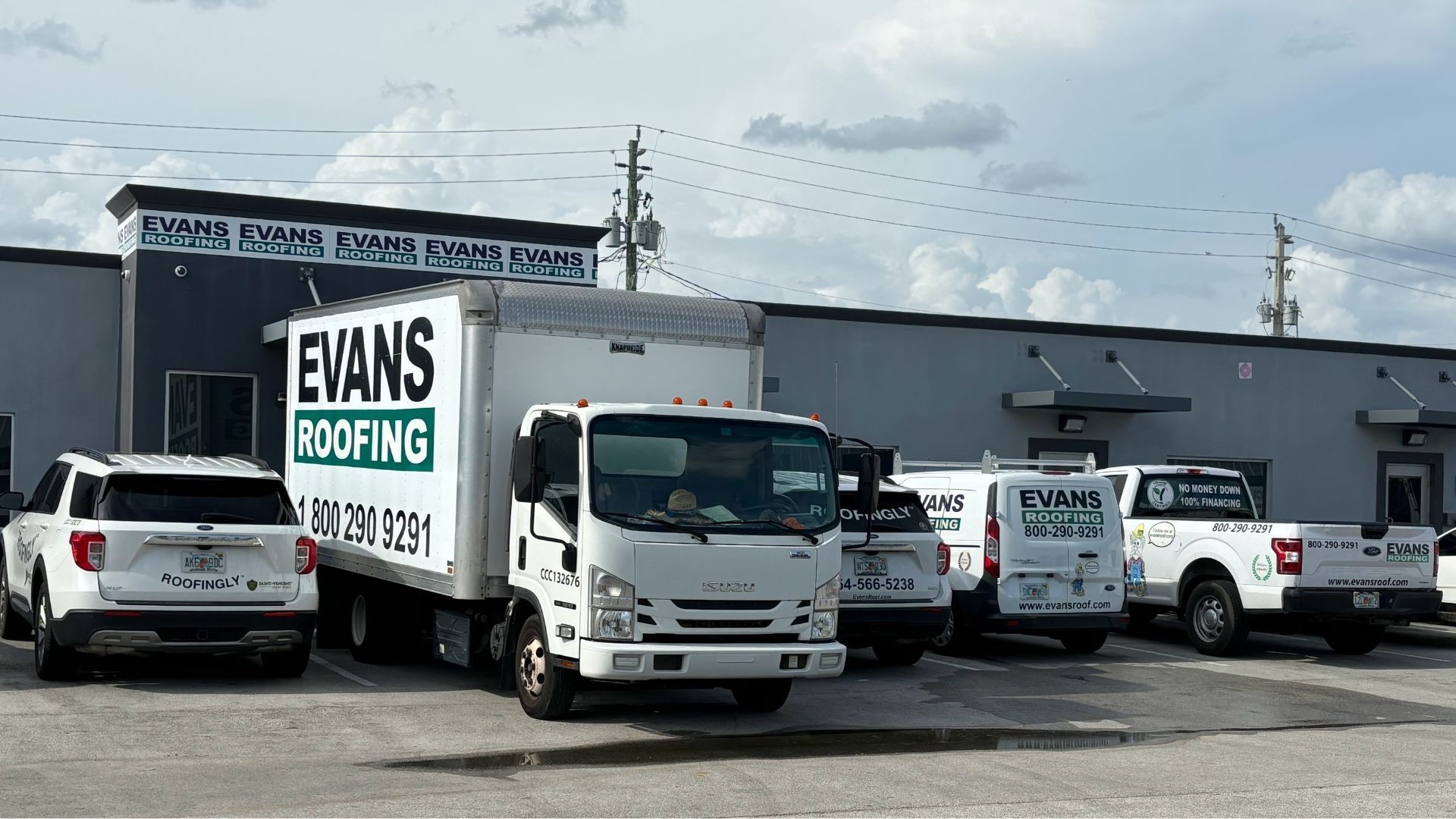 A row of evans roofing trucks are parked in front of a building.