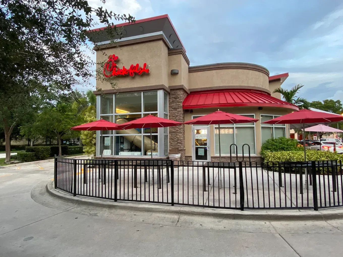 Chick-fil-A restaurant with red umbrellas, drive-thru, and patio seating, tan building with red trim.
