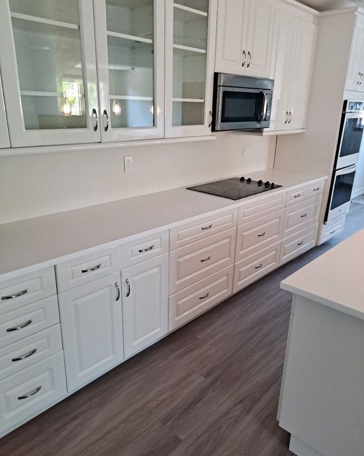 A kitchen with white cabinets , drawers , a stove and a microwave.