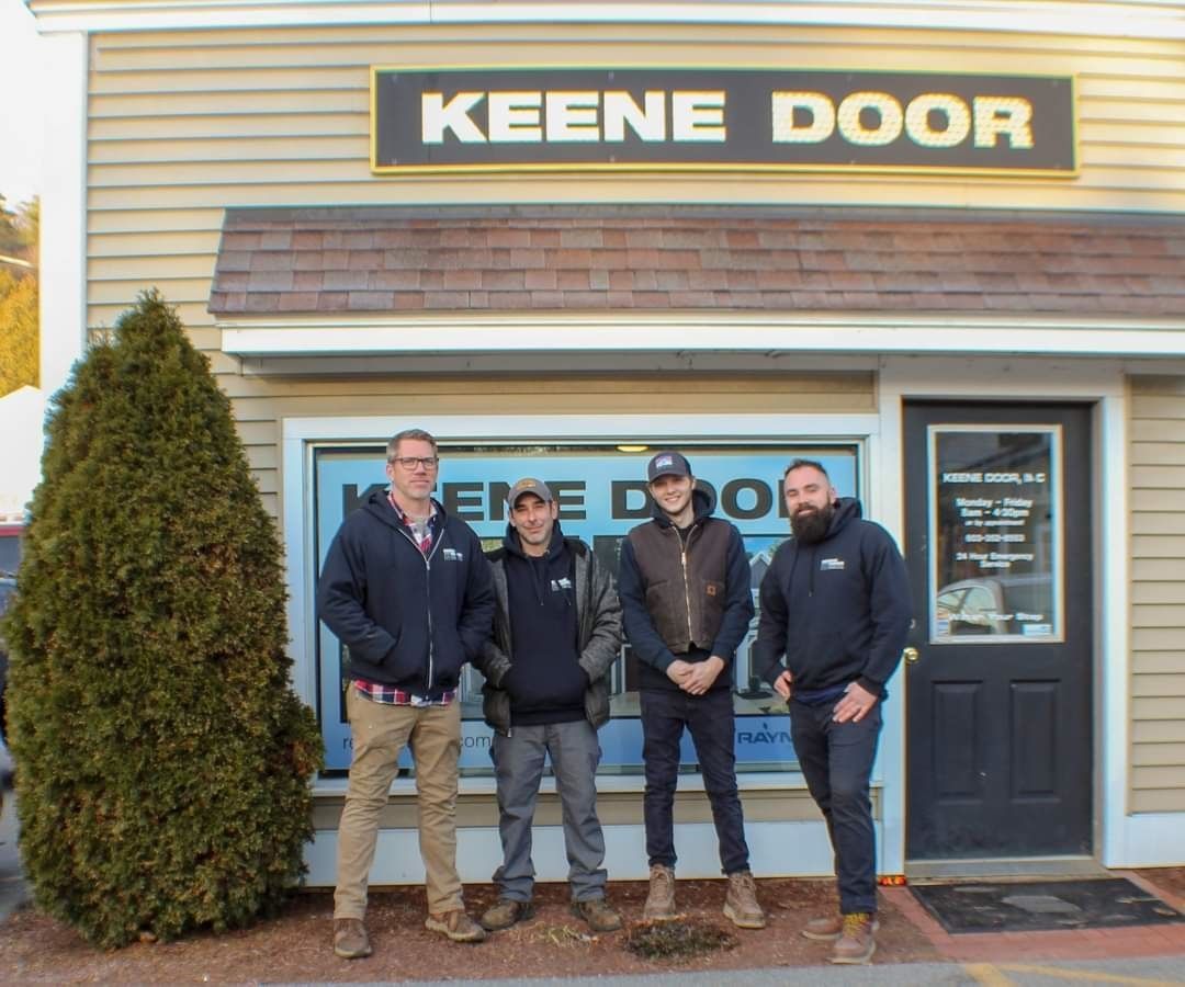 A group of men standing in front of a building that says keene door