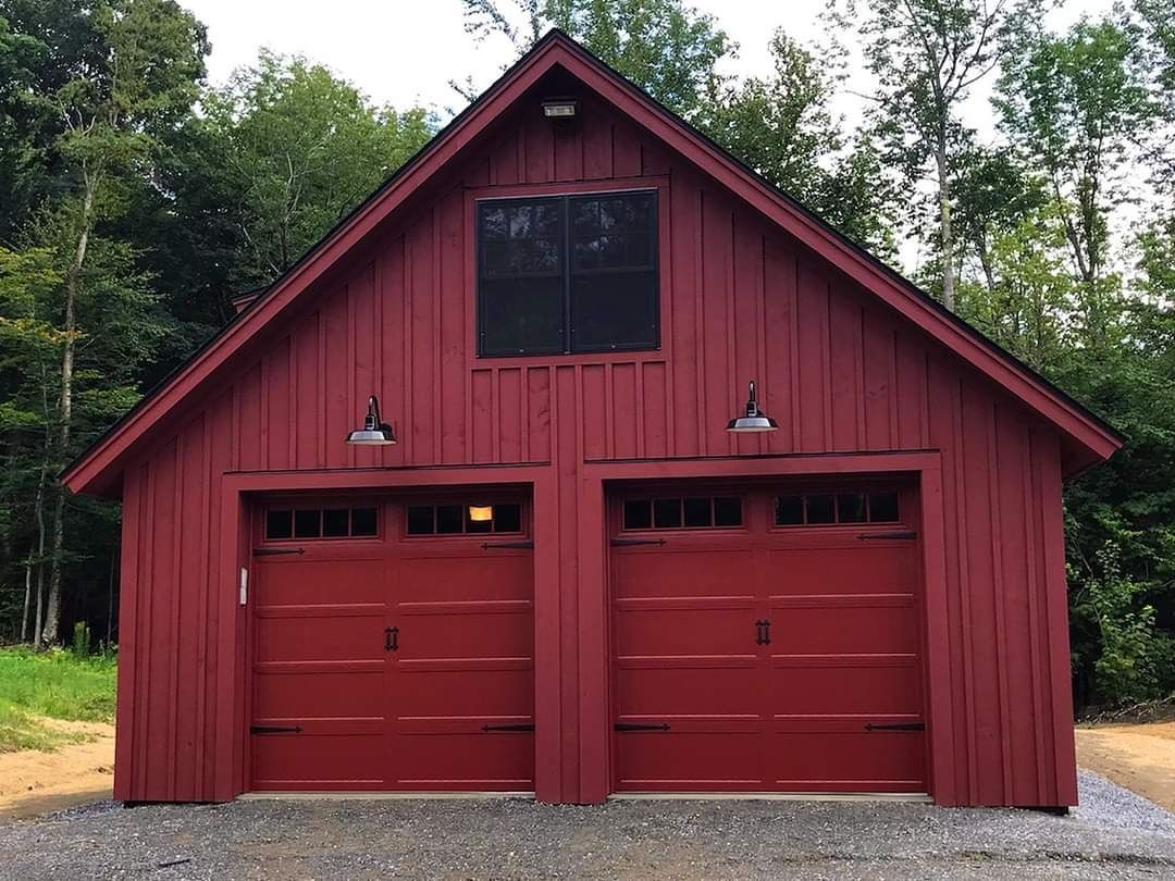 A red garage with two red garage doors and a black roof.