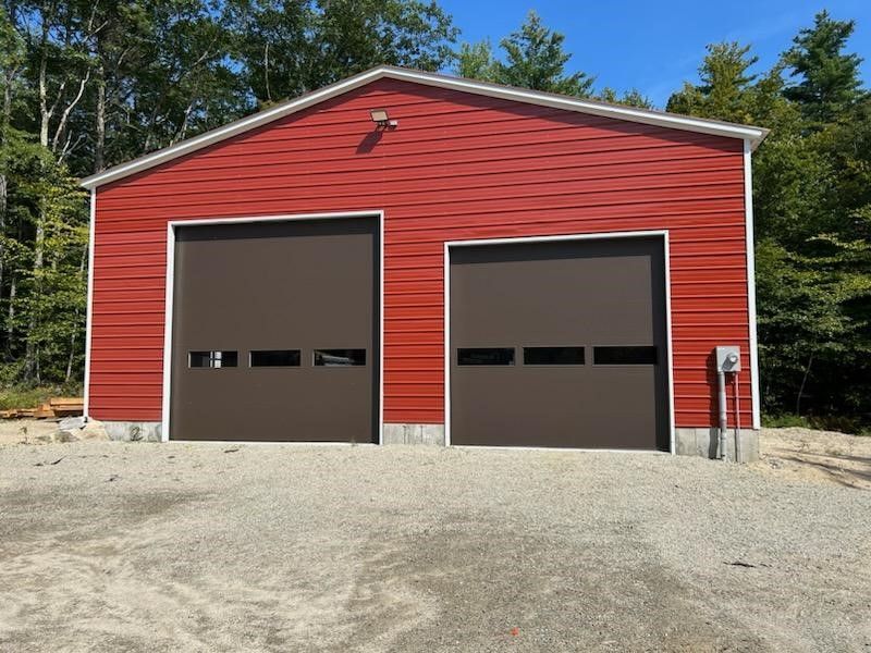 A red garage with two brown garage doors is surrounded by trees.