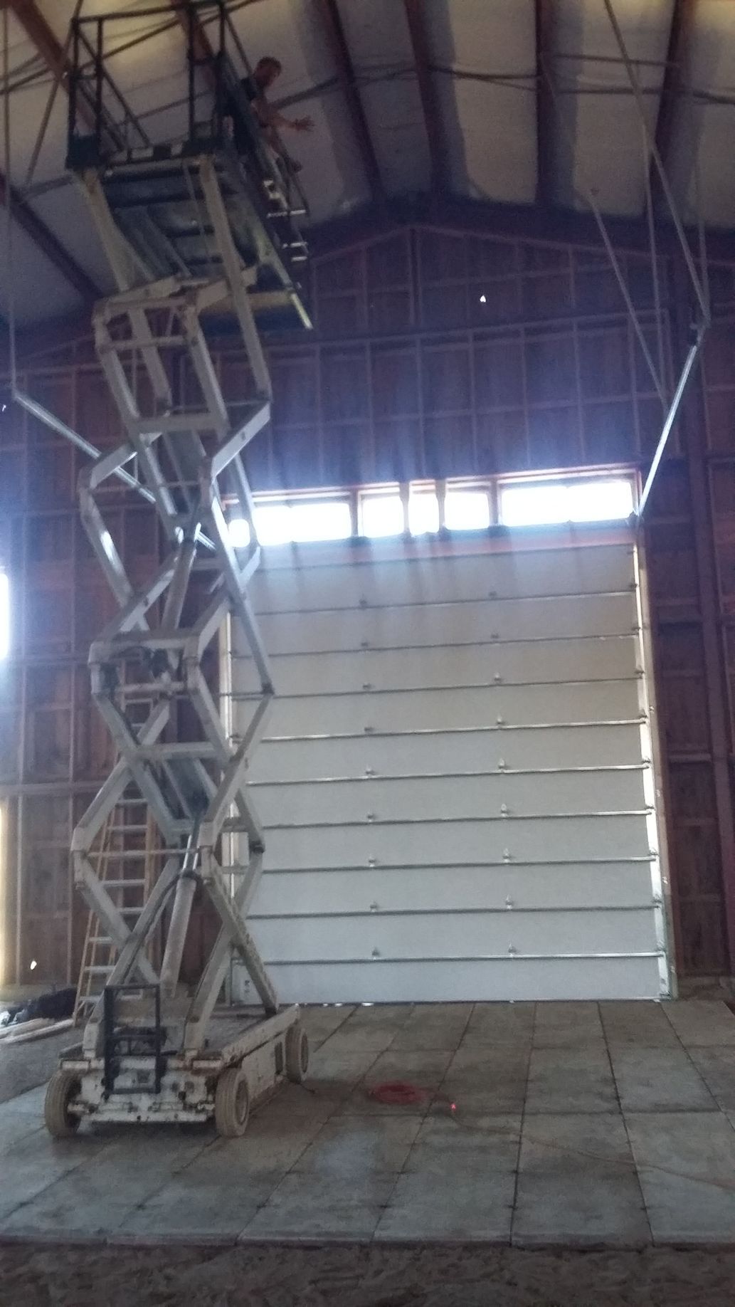 A scissor lift is sitting in front of a large garage door.