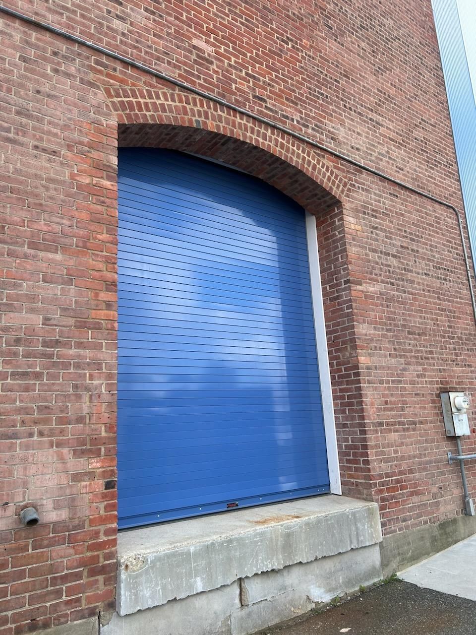 A blue garage door is on the side of a brick building.