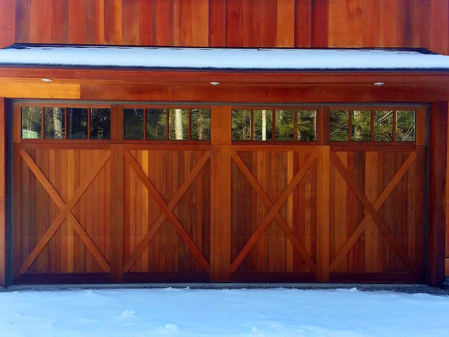 A wooden garage door is sitting in the snow on the side of a house.