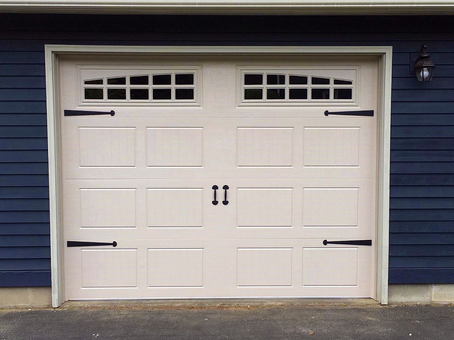 A white garage door with black handles is on a blue house.