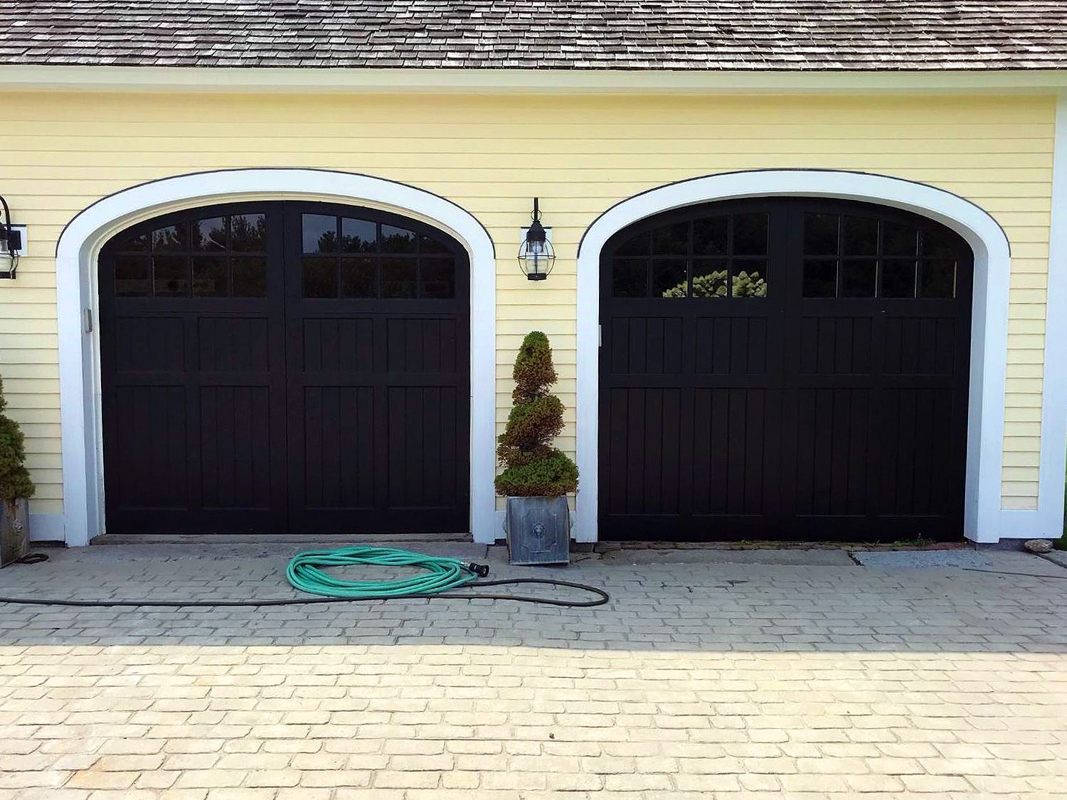 A yellow house with black garage doors and a green hose
