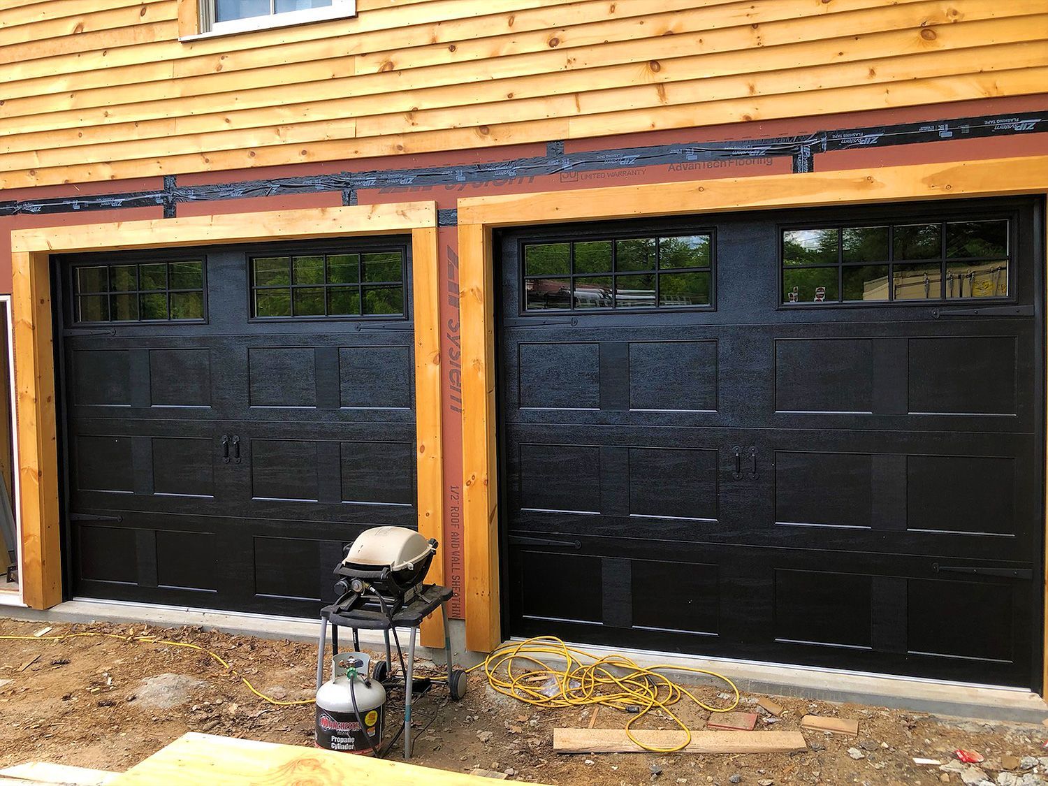 A black garage door is sitting next to a wooden house.