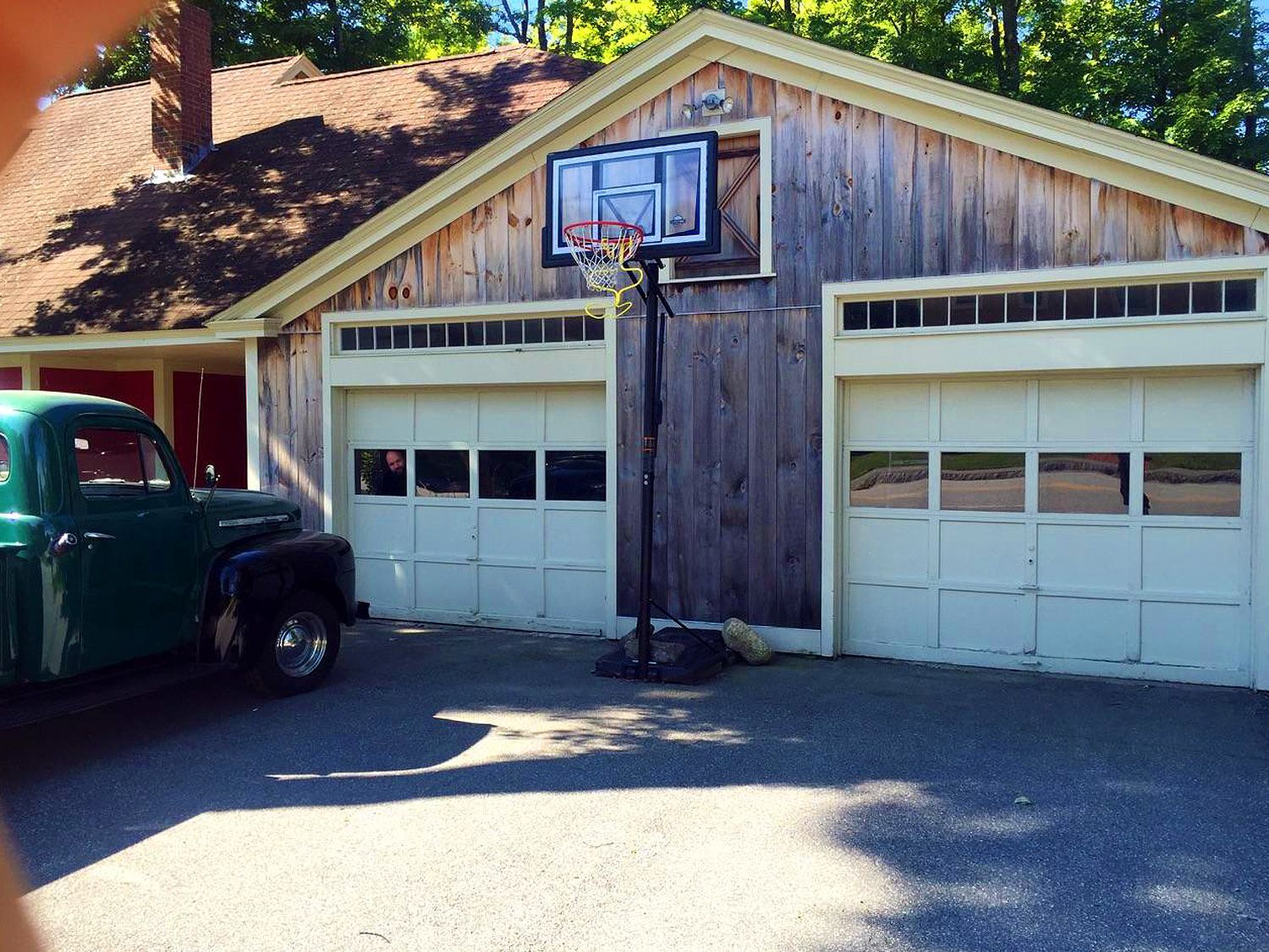 A green truck is parked in front of a garage with a basketball hoop on the side.