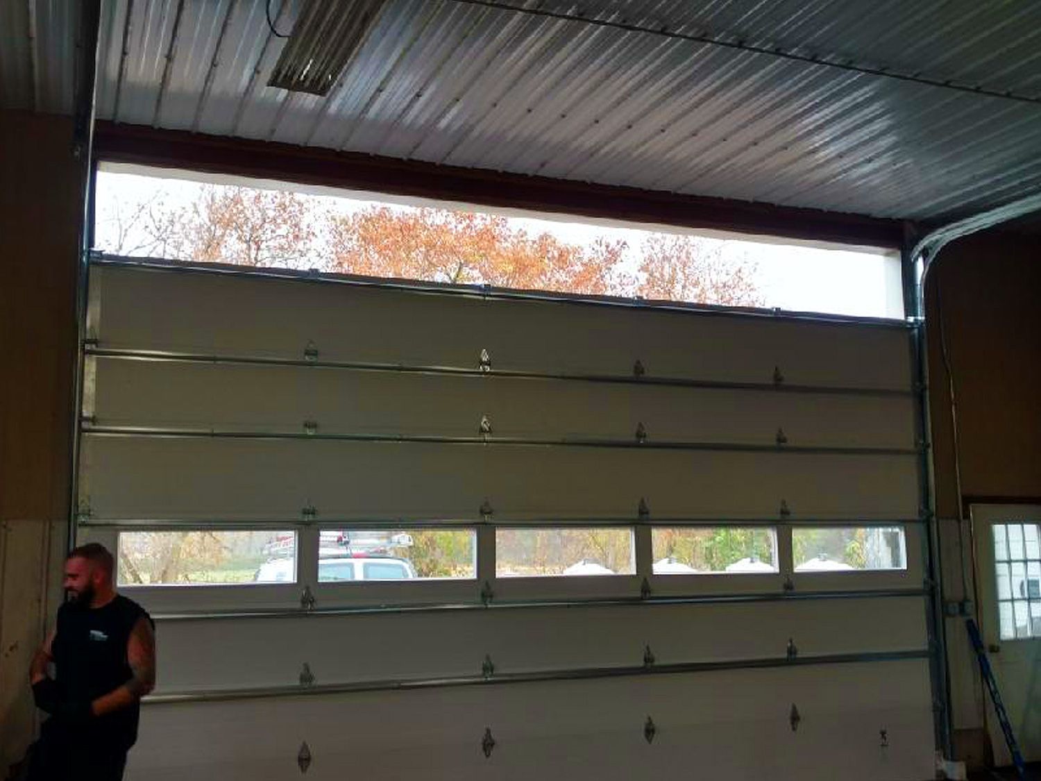 A man is standing in a garage with a large garage door open.