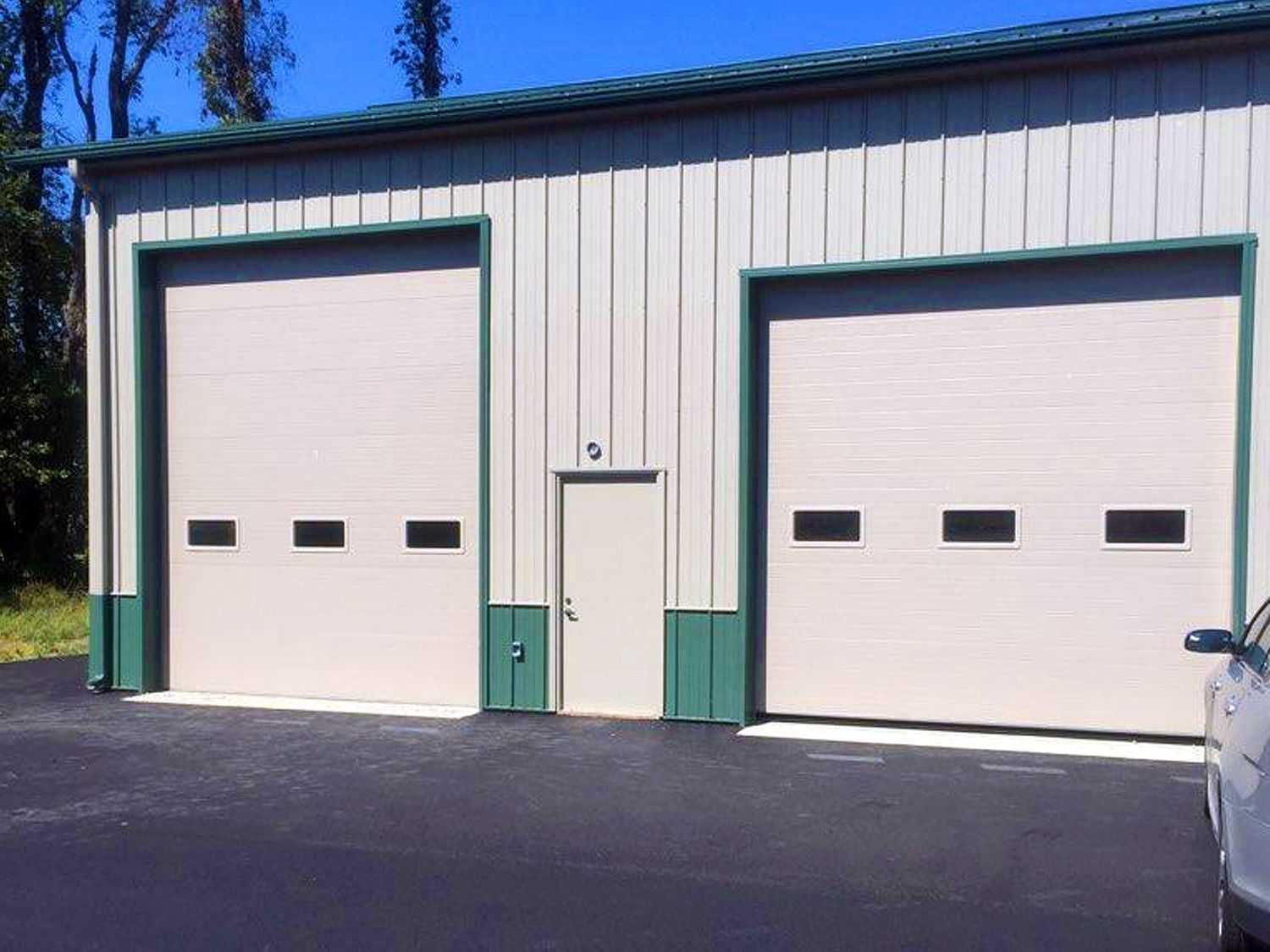 A car is parked in front of a garage with two garage doors