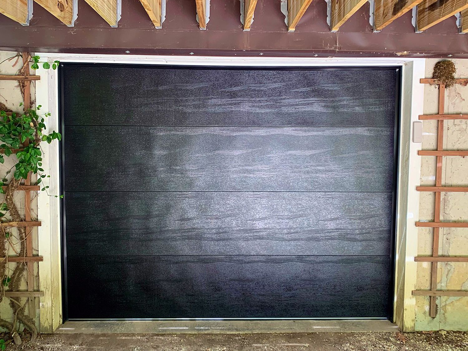 A black garage door with a wooden trellis on the side of it.