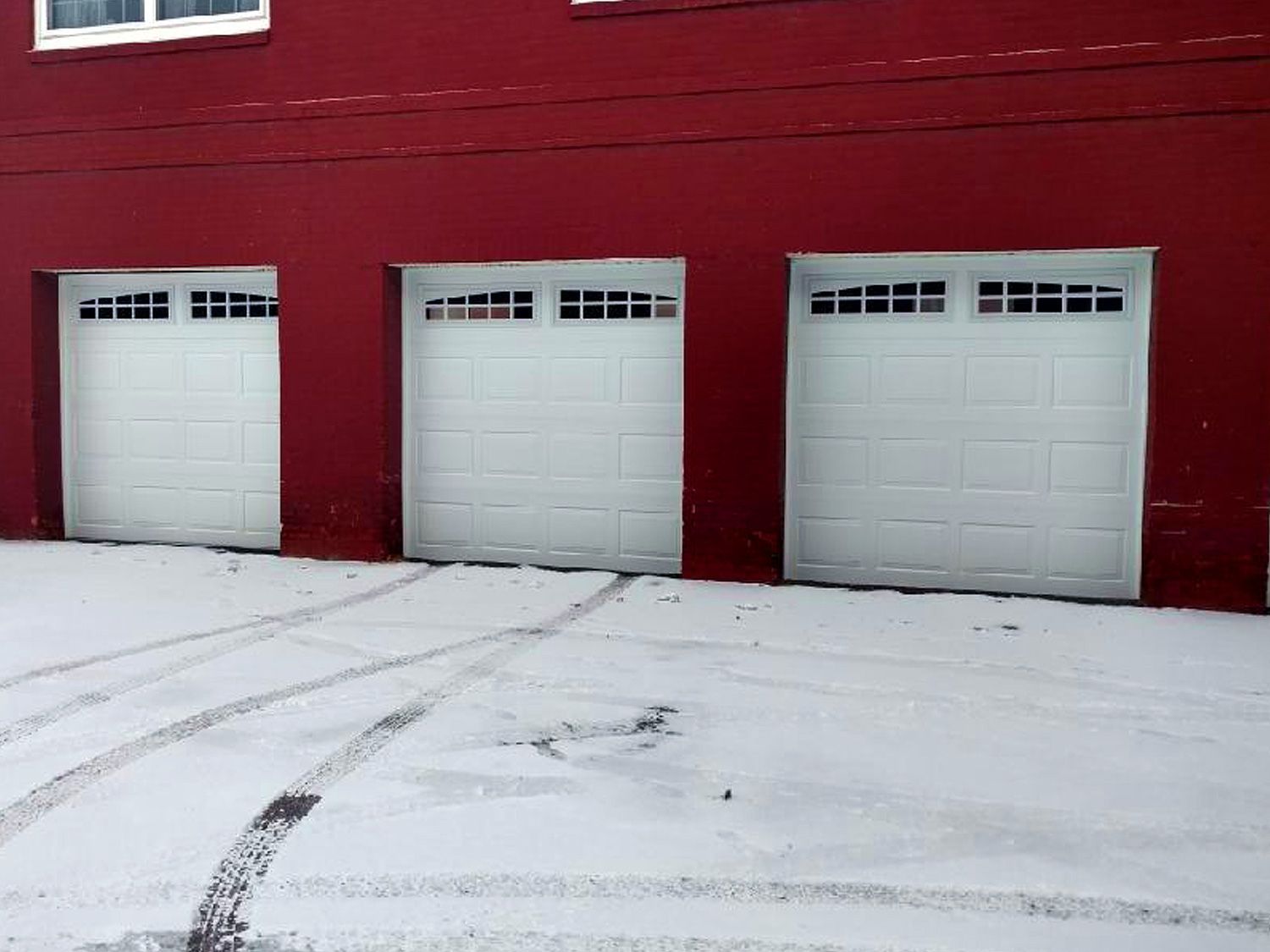 Three white garage doors are lined up in front of a red building.