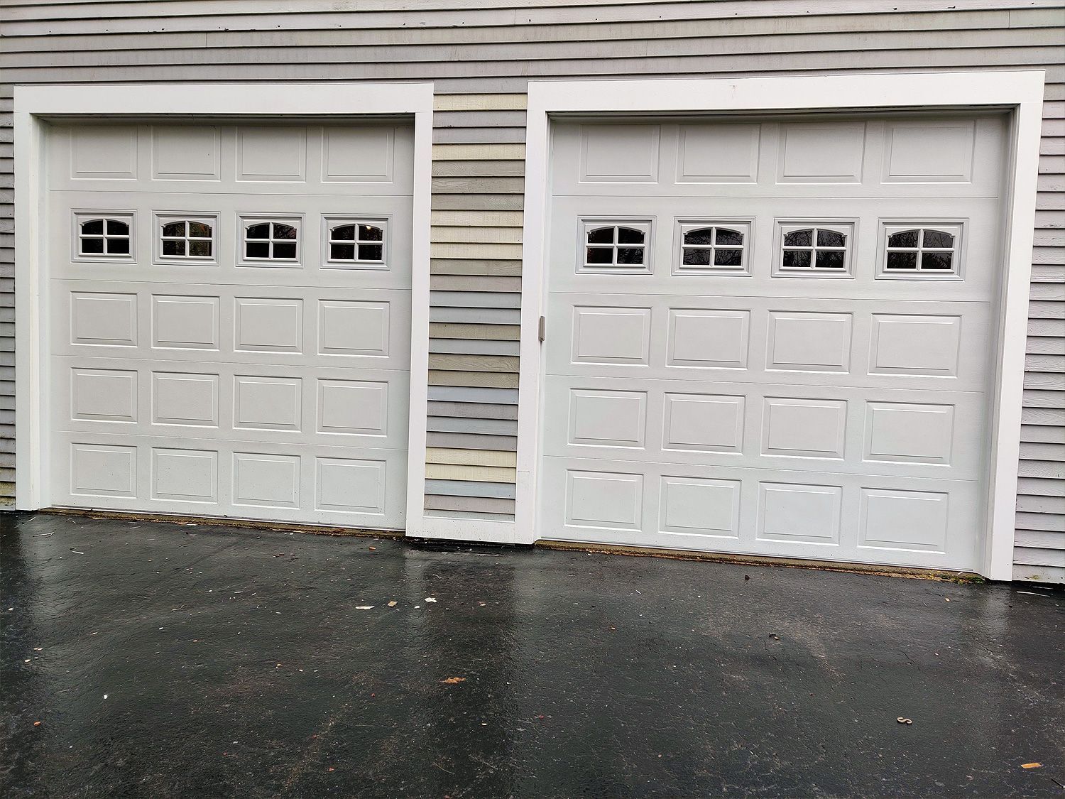 Two white garage doors are sitting next to each other on the side of a house.