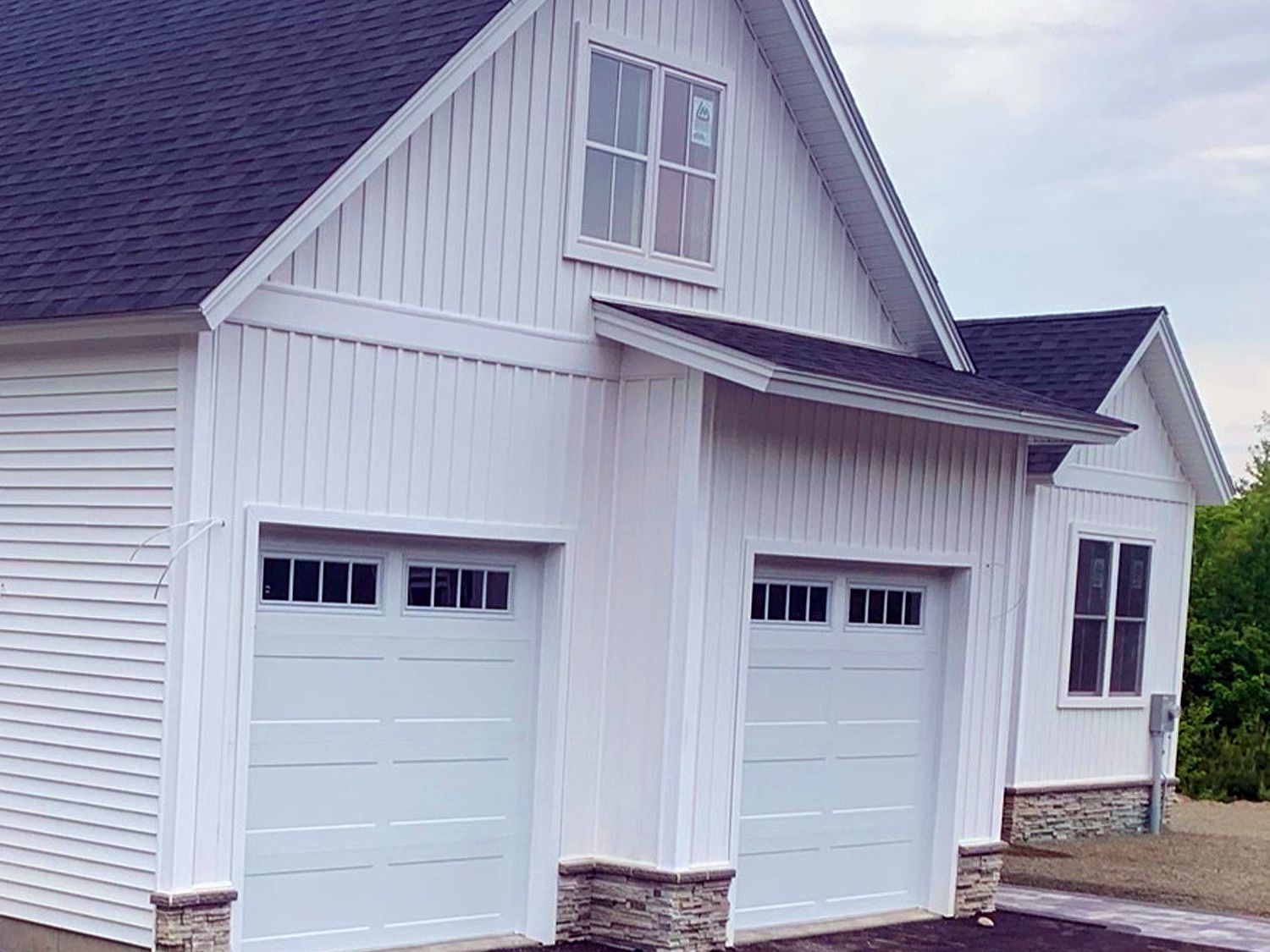 A white garage with two white garage doors and a black roof.