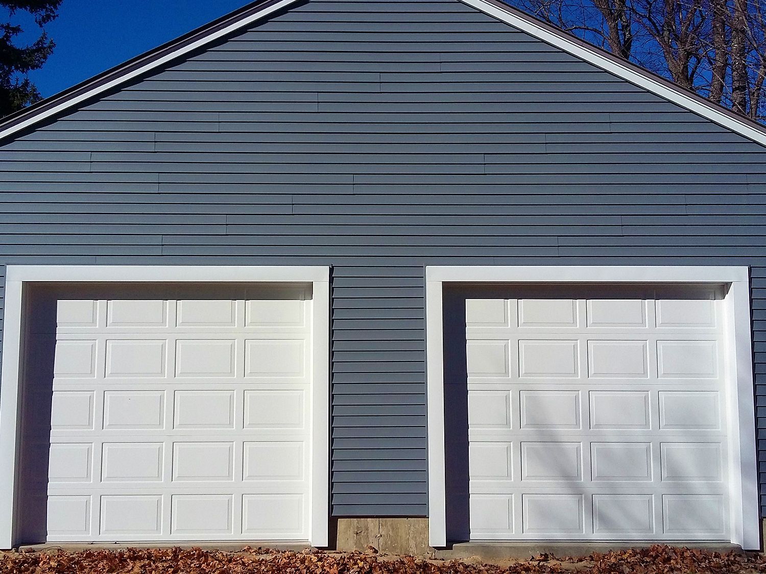 Two white garage doors on a house with a blue siding